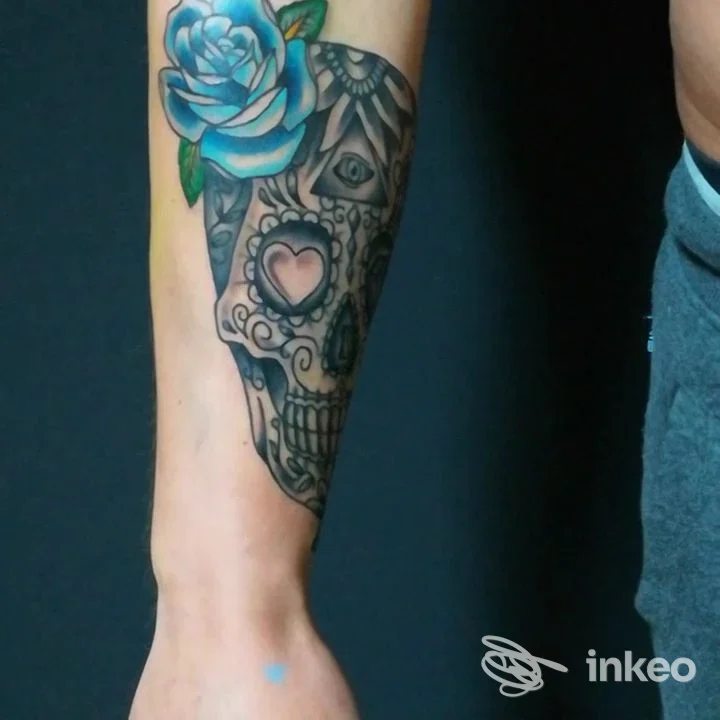 Avambraccio con tatuaggio a teschio ornamentale e rosa azzurra, fotografia inviata da La Sartoria Tattoo, Colle di Val d'Elsa.