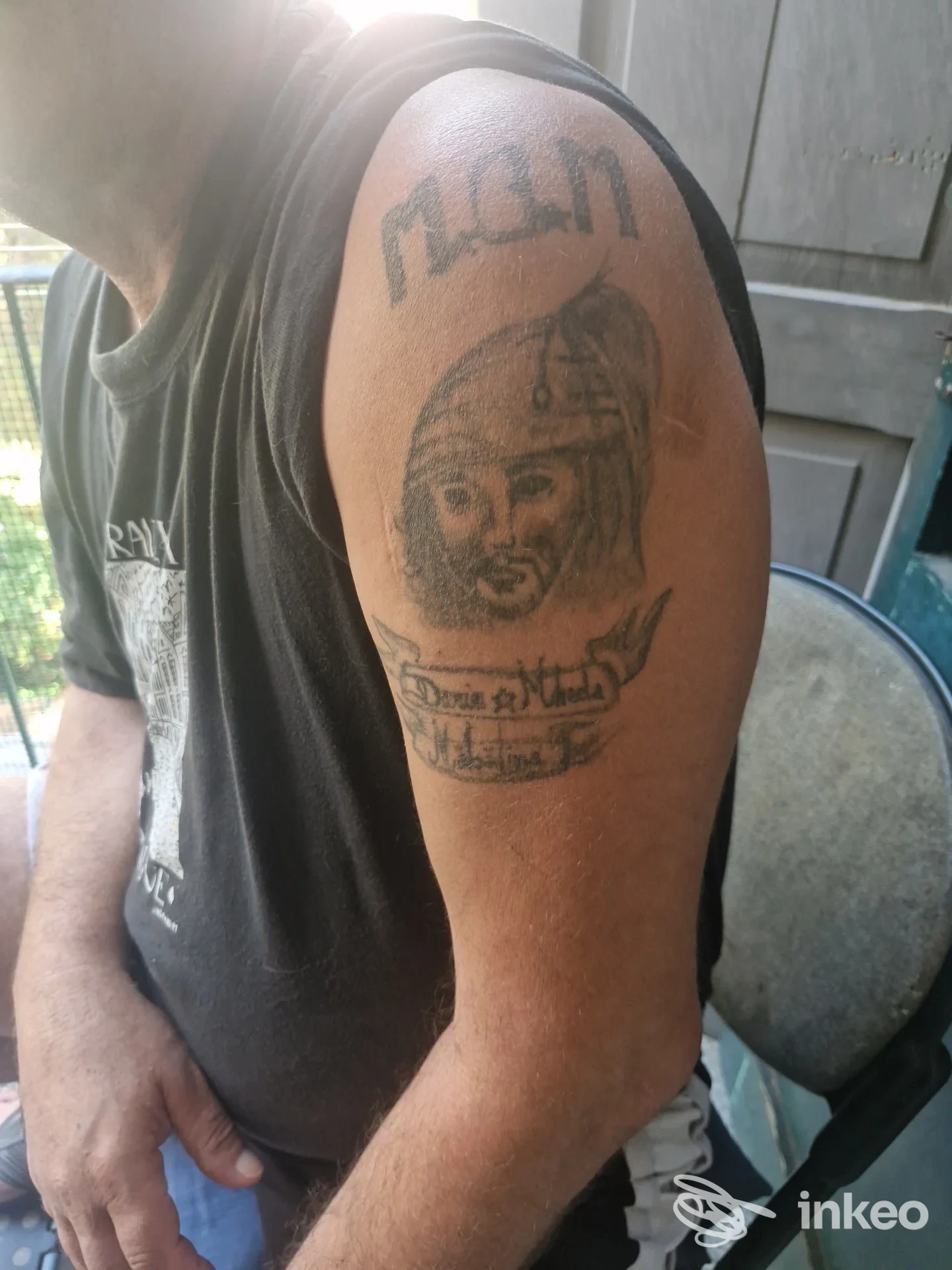 Tatuaggio in nero sul deltoide con volto elmo e banner, foto inviata da Lacrimanera Tattoo Saloon, Firenze.