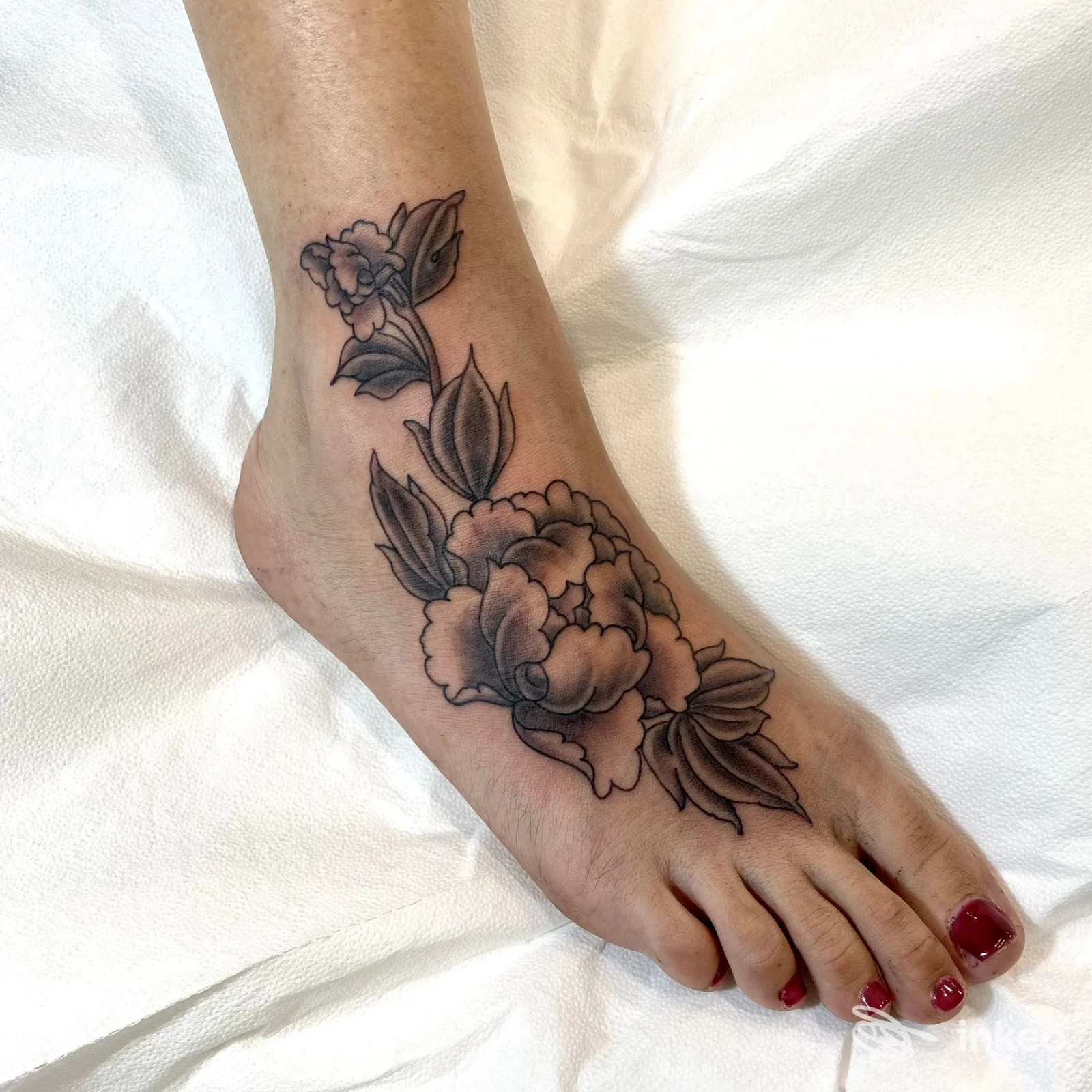 Tatuaggio floreale in bianco e nero sul dorso del piede e caviglia, foto dello studio Luci Bart Tattoo - Tatuaggi a Follonica.
