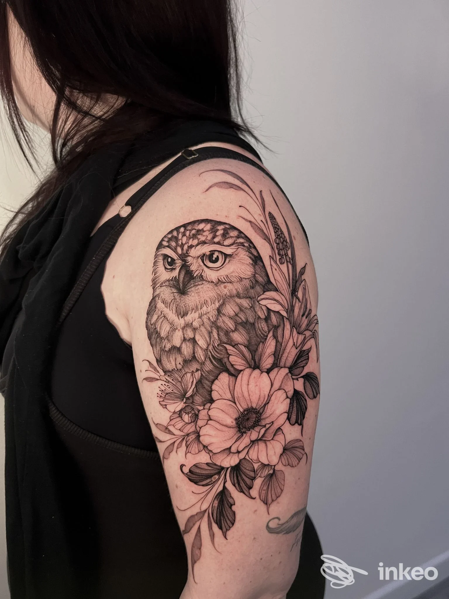 Tatuaggio presso Melograno Tattoo Studio a Firenze: civetta e fiori a inchiostro nero sull'alto braccio.