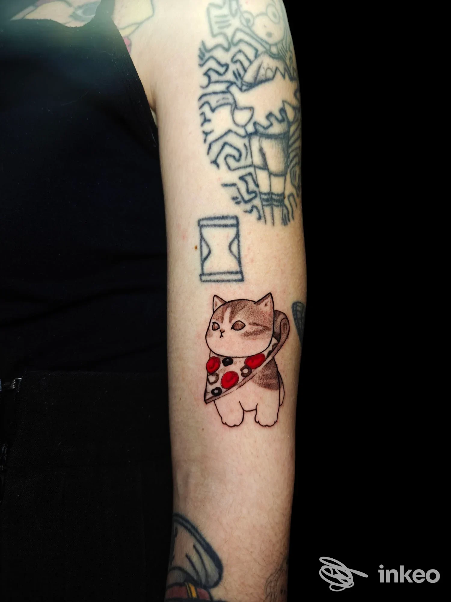 Avambraccio tatuato con un gatto stilizzato che tiene una fetta di pizza, foto inviata da Melograno Tattoo Studio, Firenze.