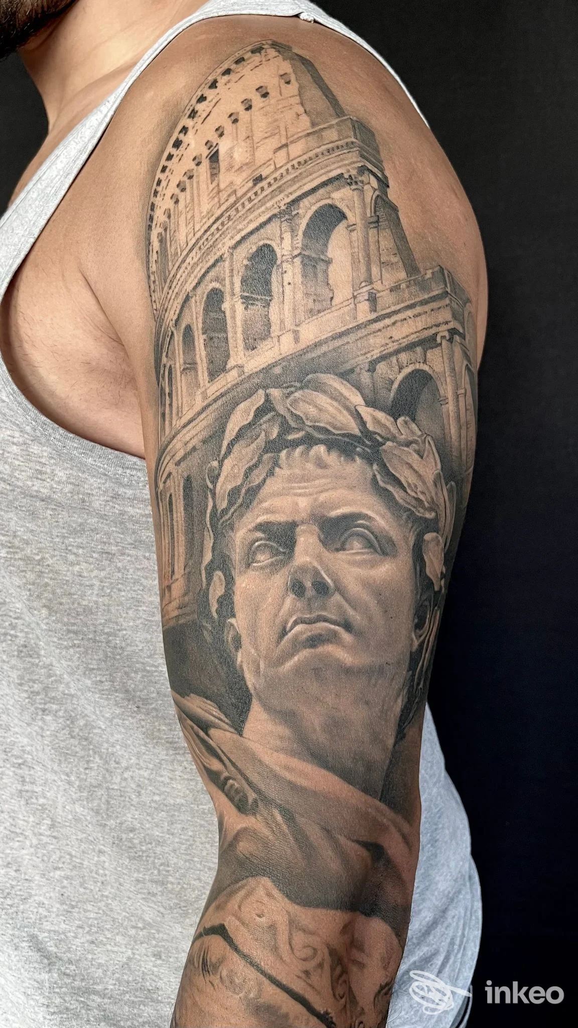 Tatuaggio realistico in bianco e nero sul braccio superiore raffigurante il Colosseo e un busto classico, foto fornita da Nocturno Tattoo, Cecina.