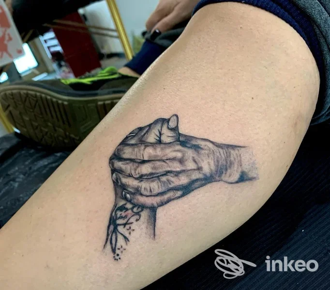 Tatuaggio realistico in bianco e nero di due mani che si stringono sul braccio, foto da NoireInkTattooStudio a Pontedera.