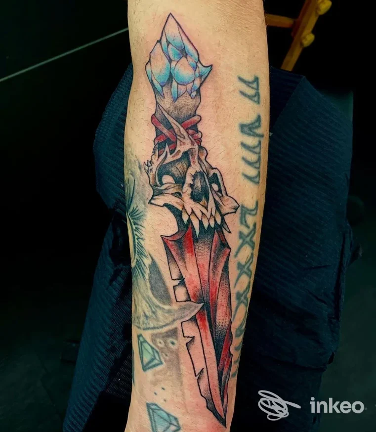 Tatuaggio a pugnale e cranio su avambraccio eseguito presso NoireInkTattooStudio, Pontedera; colori rossi e blu in primo piano.