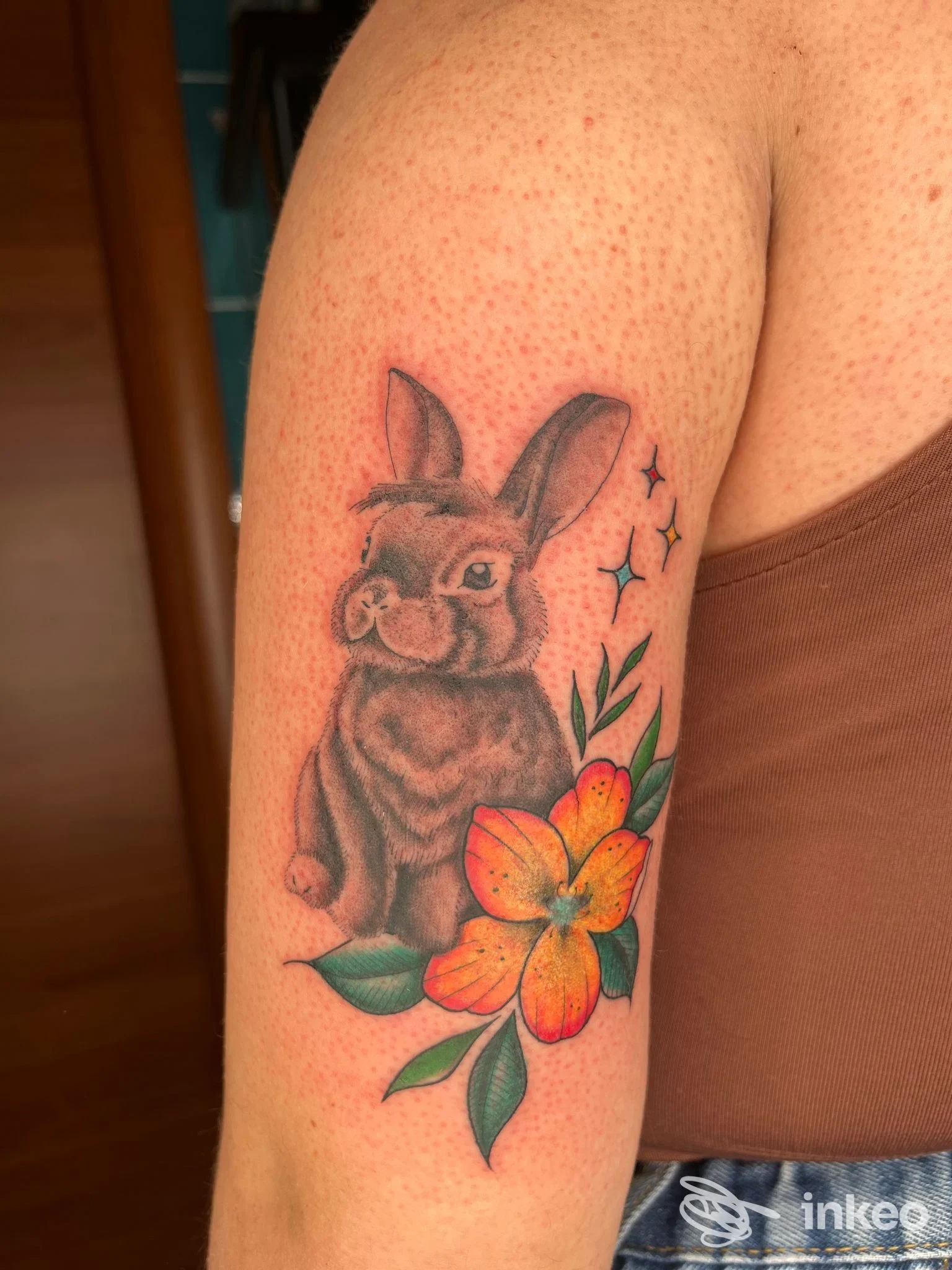 Tatuaggio su braccio superiore con coniglio grigio e fiore arancione, foto fornita da NEDO TATTOO, Camaiore.