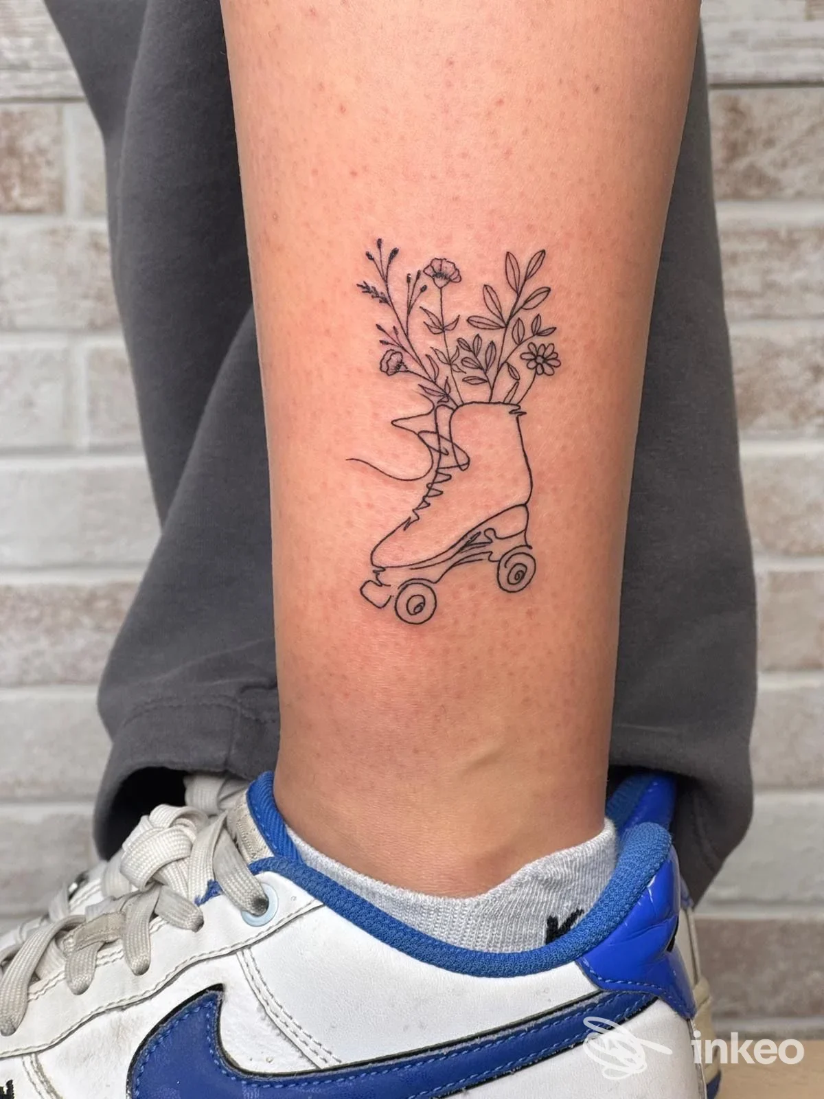 Tatuaggio lineare di un pattino a rotelle con fiori sulla parte inferiore della gamba, foto fornita da Nora Tattoo Studio, Scandicci.