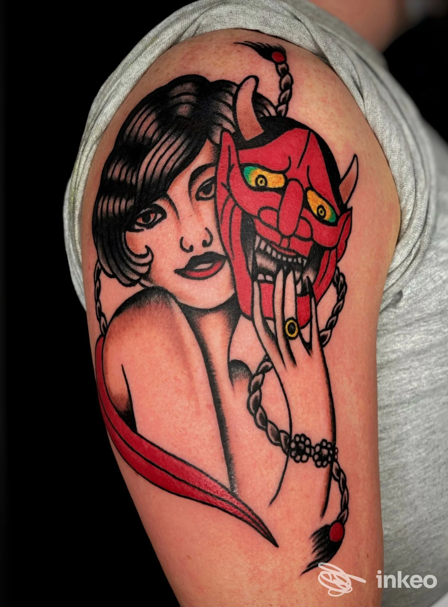 Tatuaggio neo-traditional sul bicipite con donna che tiene una maschera rossa, Officina 95 tattoo studio, Castelfranco Piandiscò.