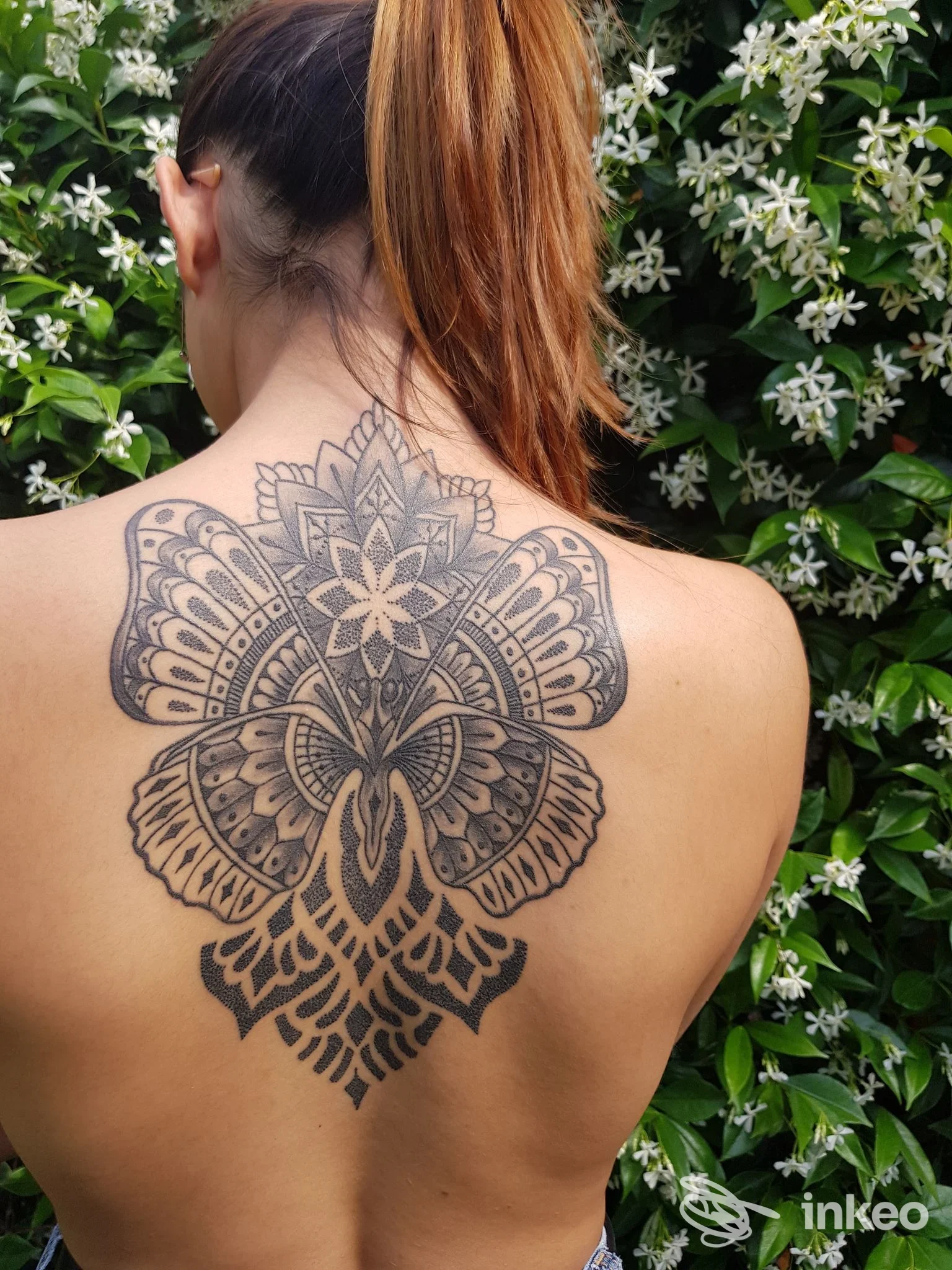 Ampio tatuaggio ornamentale a mandala sulla parte superiore della schiena di una donna, fotografato all'aperto. Preta Tattoo, Viareggio.