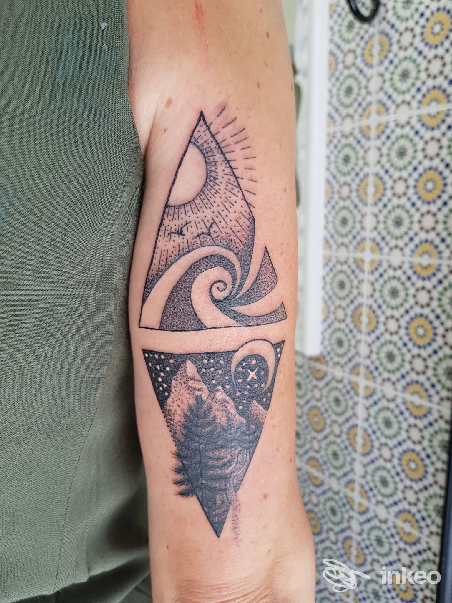 Tatuaggio geometrico a inchiostro nero su avambraccio con motivi sole, onde e paesaggio montano; foto inviata da Preta Tattoo, Viareggio.