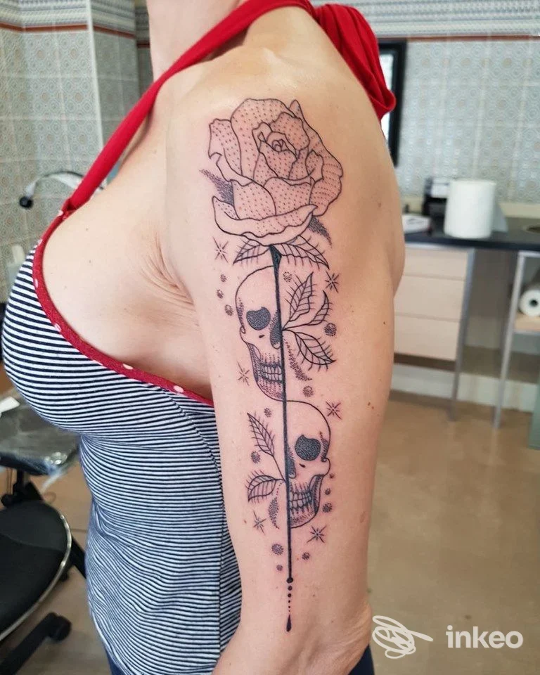 Tatuaggio linework e dotwork sul braccio superiore con rosa e teschi, foto scattata nello studio Preta Tattoo a Viareggio.