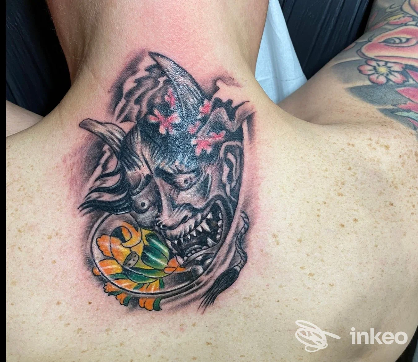 Tatuaggio a colori di maschera demoniaca sulla parte superiore della schiena, realizzato da Red & Black Tatoo Studio ad Arezzo.