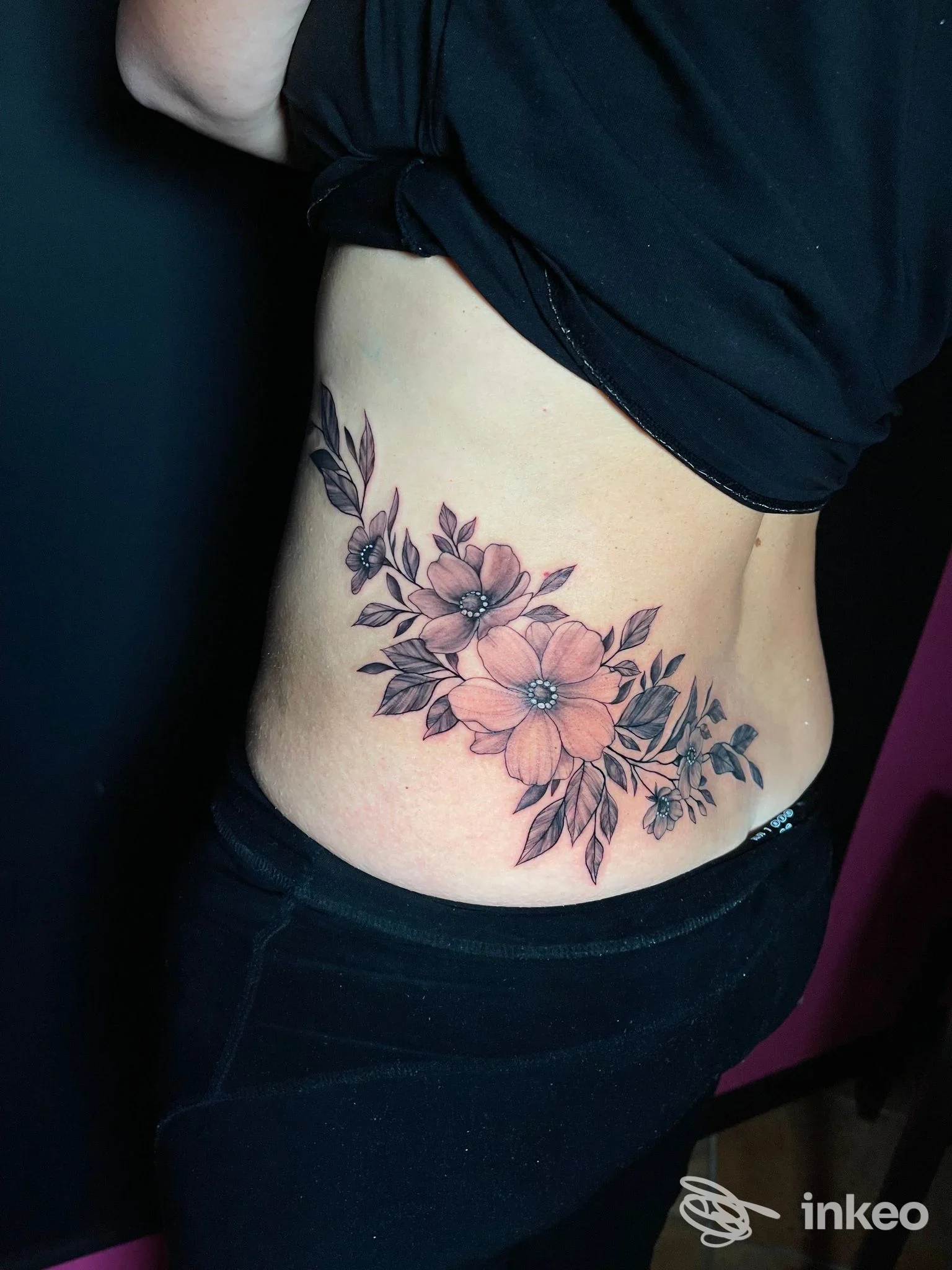 Tatuaggio floreale sul fianco realizzato da Sara D Tattoo Studio, Pontedera: fiori rosa e foglie verdi in posizione laterale sulla pelle.