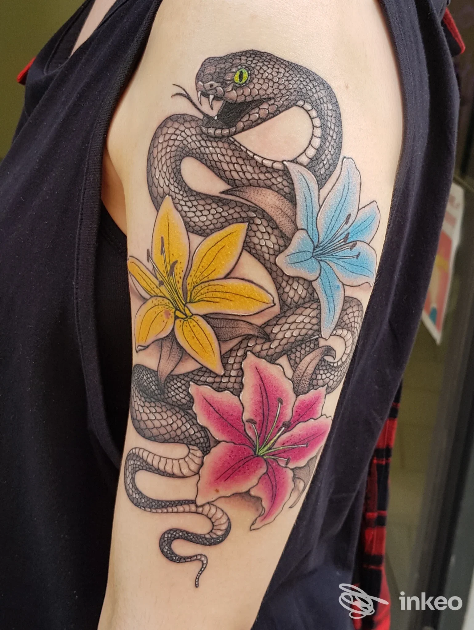 Tatuaggio su braccio superiore con serpente nero e tre gigli colorati, foto inviata da Sphynx Tattoo - Tatuaggi Pisa, Pisa.