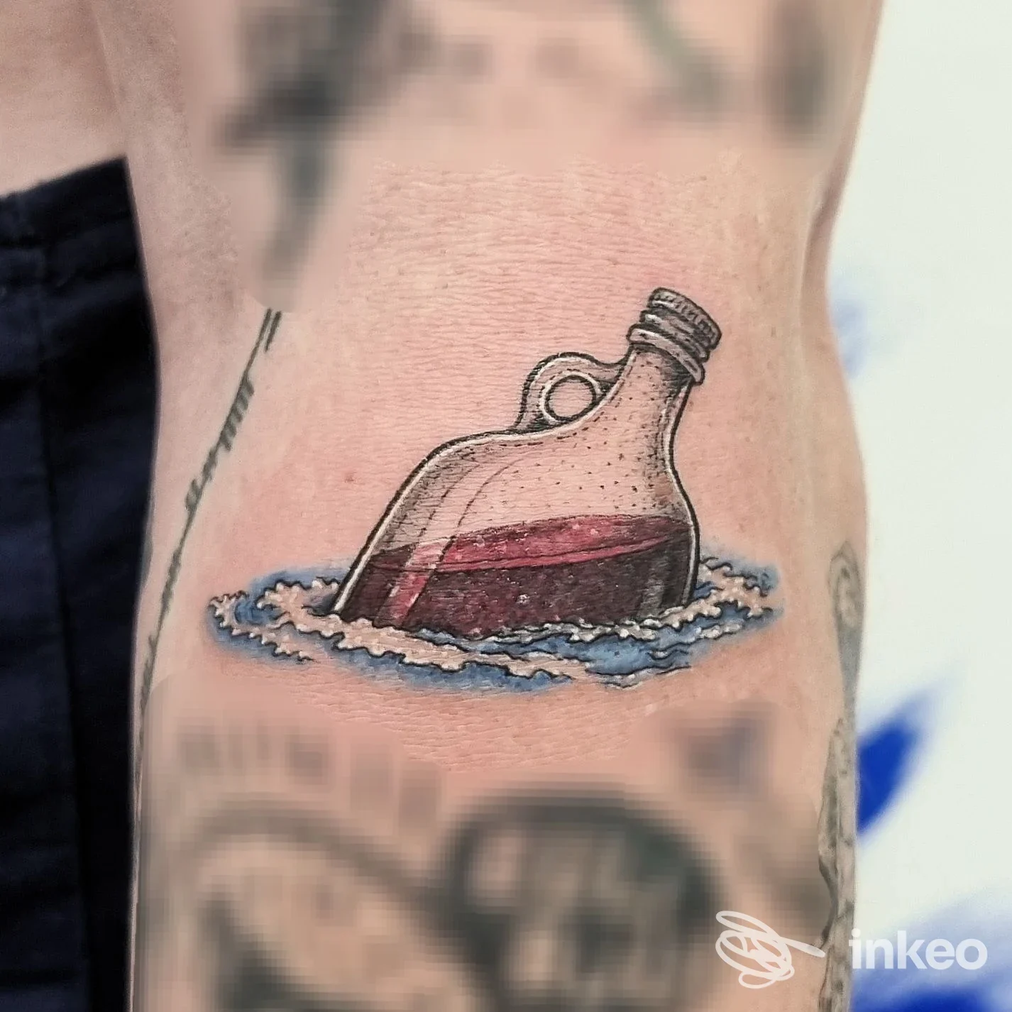 Tatuaggio colorato di una bottiglia che galleggia su onde, fotografato sull'avambraccio; immagine per Sphynx Tattoo - Tatuaggi Pisa, Pisa.