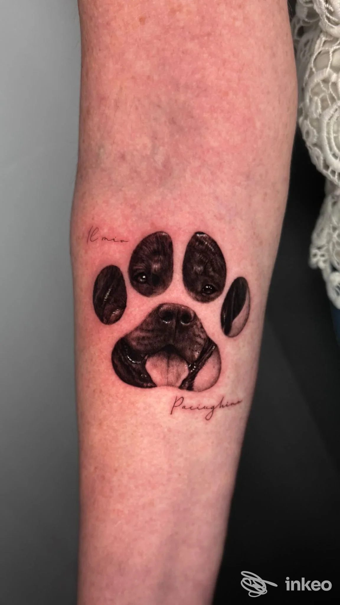 Tattoo su avambraccio raffigurante zampa di cane nera, con firma in corsivo e sfondo carne.
