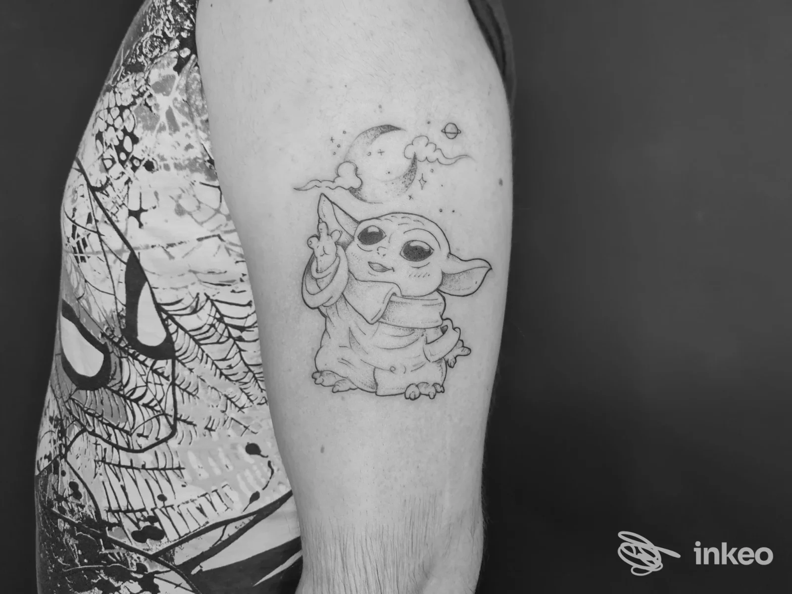 Tatuaggio in bianco e nero di Baby Yoda sul braccio superiore, foto fornita da Tattoo Shop a Massa.