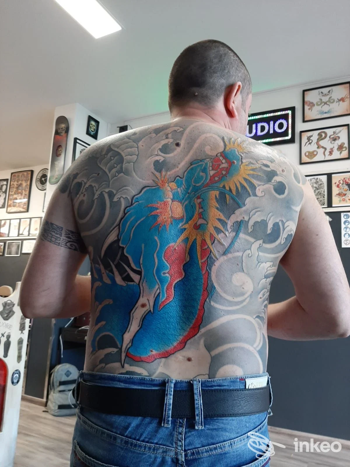Ampia schiena tatuata con onde grigie e figura centrale colorata, foto scattata nello studio The Family Tattoo a Firenze.