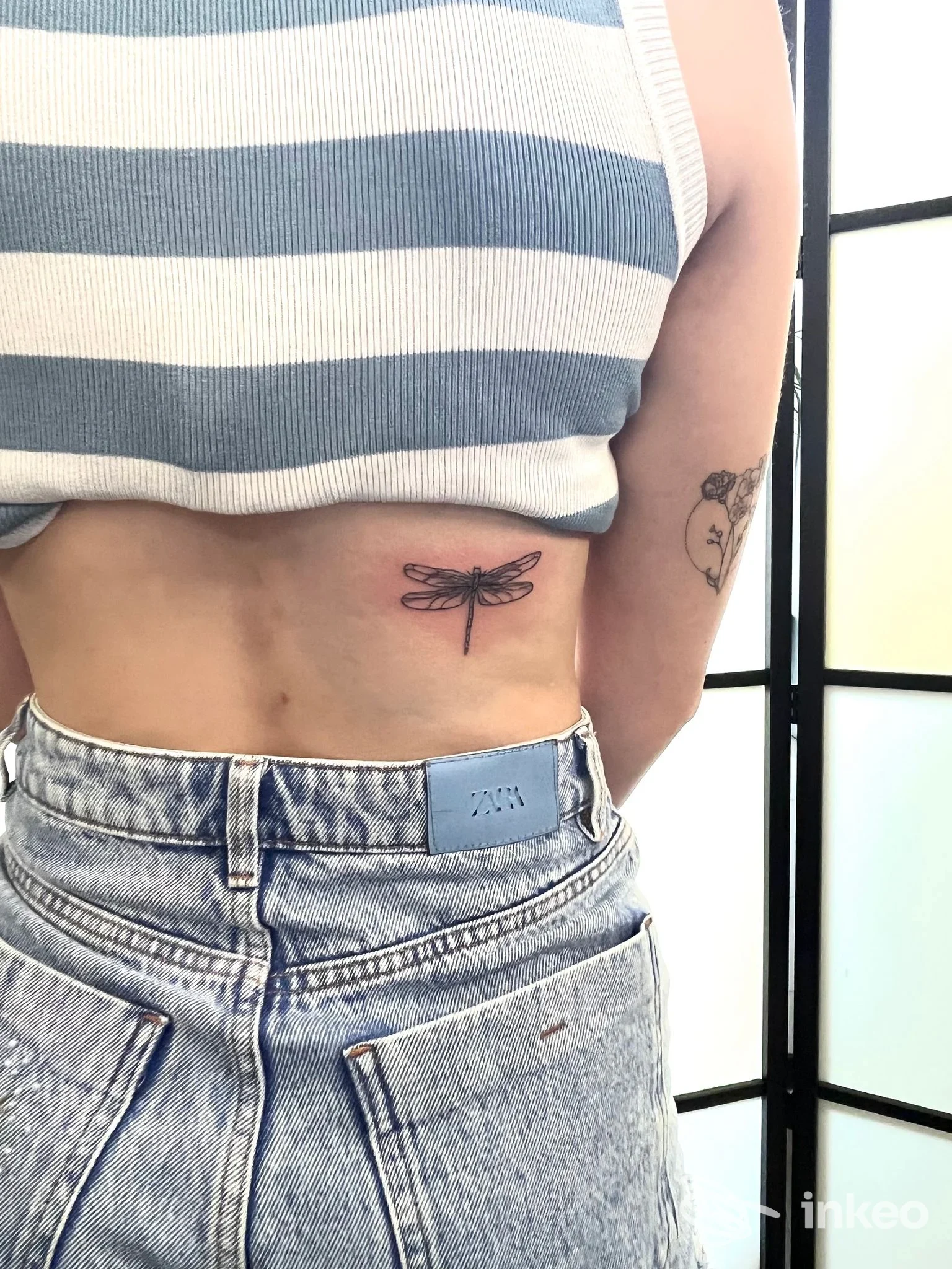Mini tatuaggio a forma di libellula visibile sull’addome di una persona, senza sovrimpressioni o watermark, in foto singola.