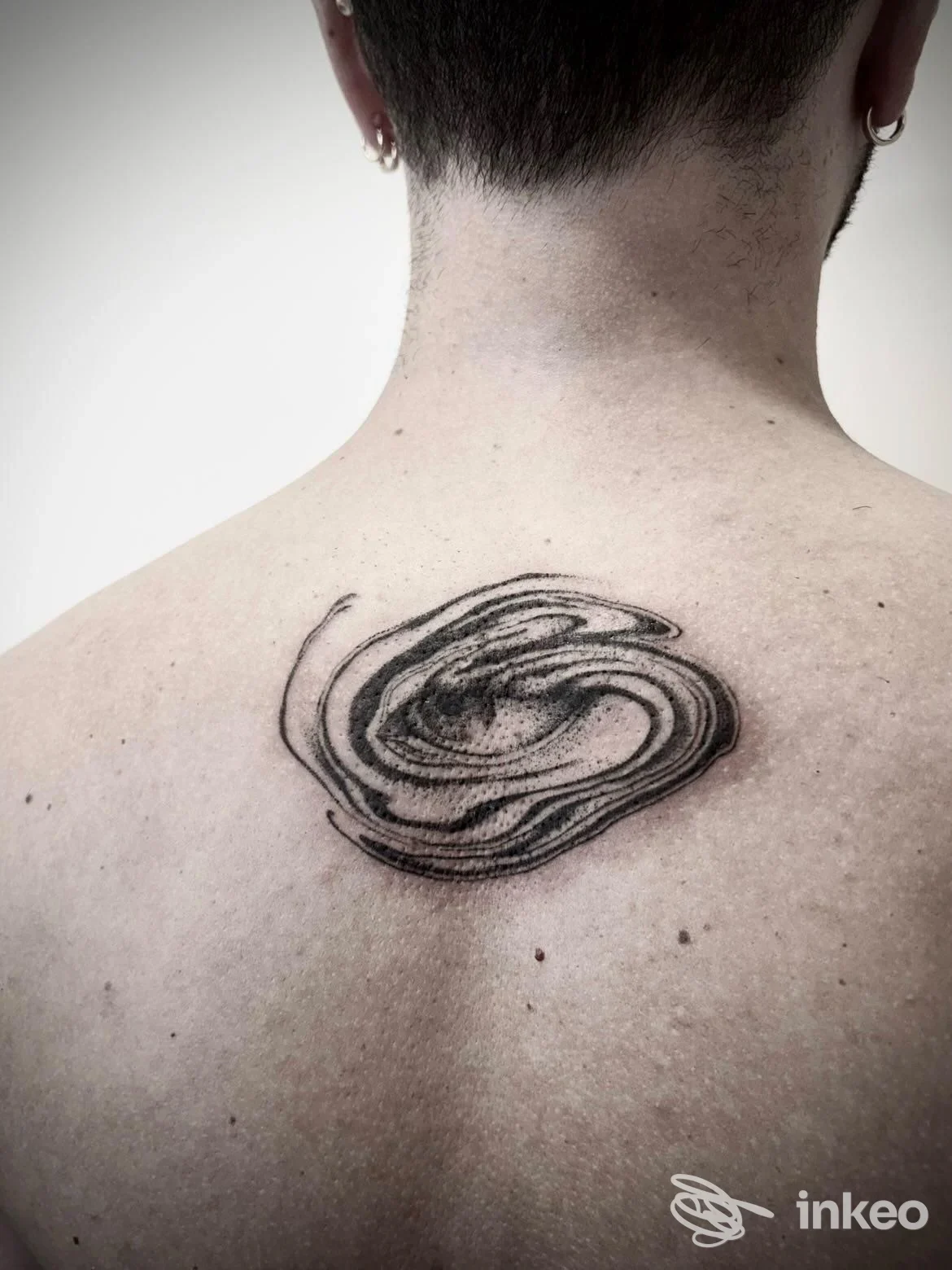 Tatuaggio astratto in nero sulla parte superiore della schiena, foto fornita da ATTITUDE Tattoo Studio a Massa.