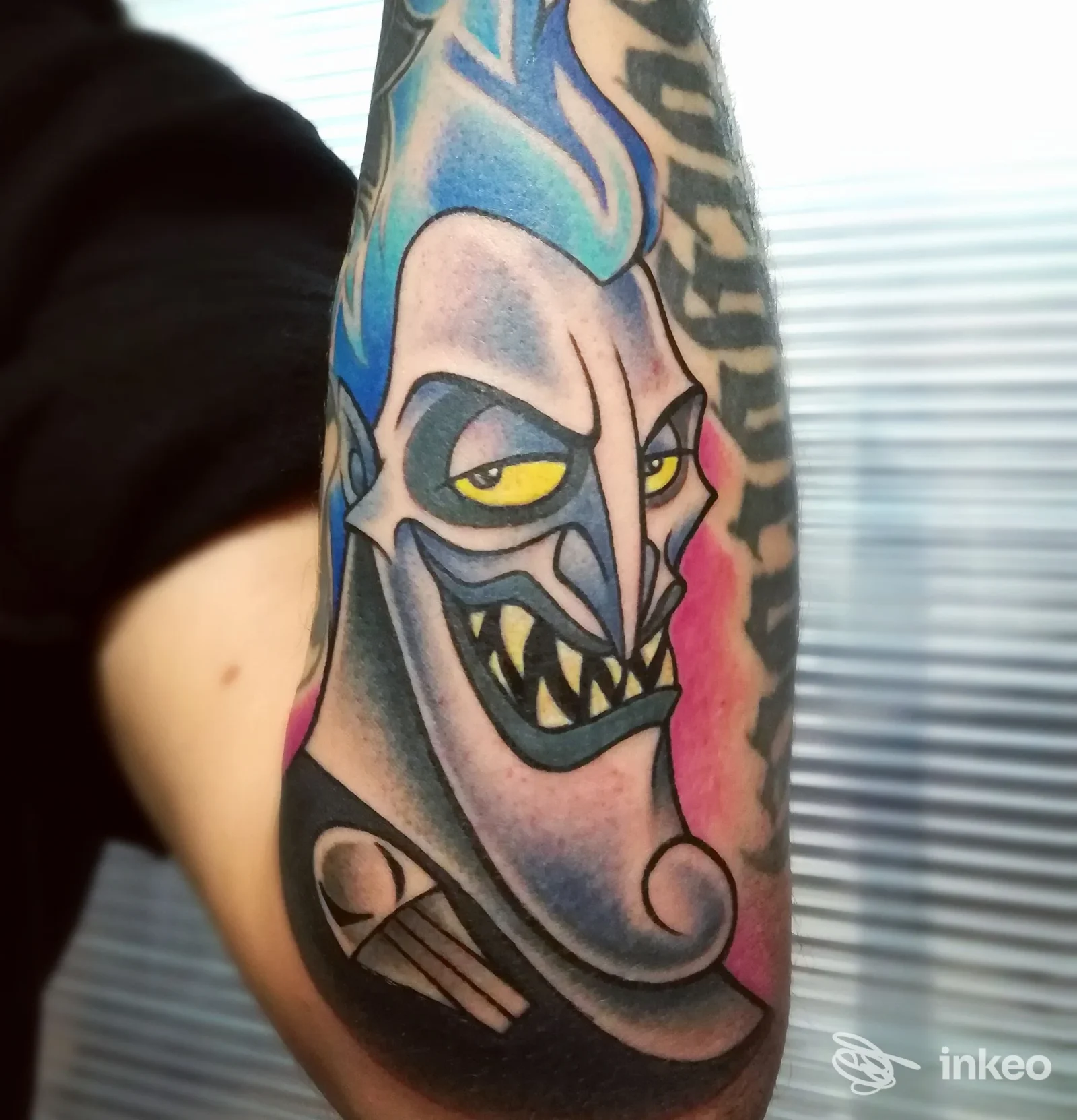 Tatuaggio colorato su avambraccio con volto mostruoso e fiamma blu, immagine fornita da Trick'r Treat Tattoo Studio, Firenze.