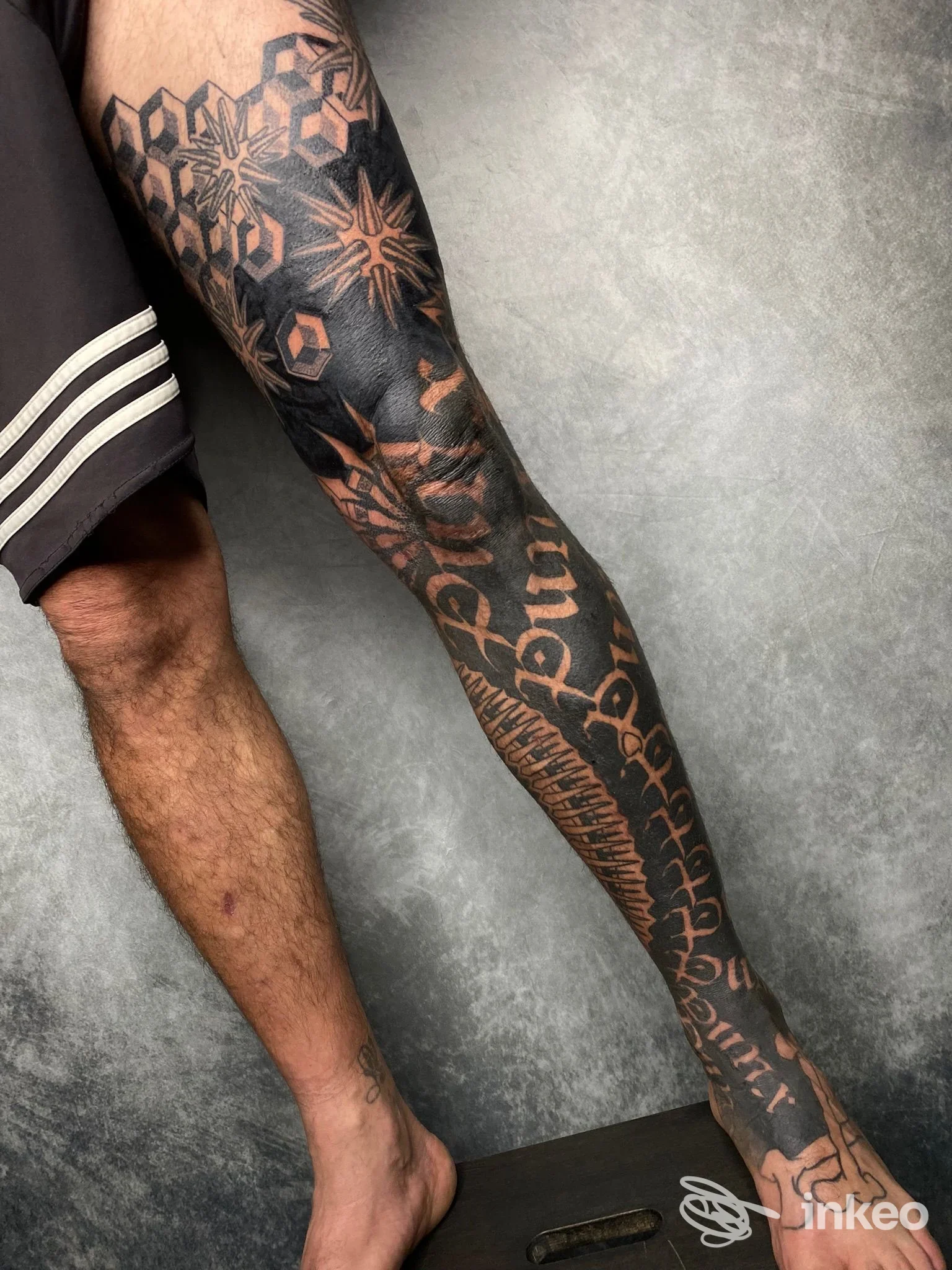 Gamba completamente tatuata con motivi geometrici, lettering e volto stilizzato, foto di AB Normal Tattoo & Piercing, Firenze.