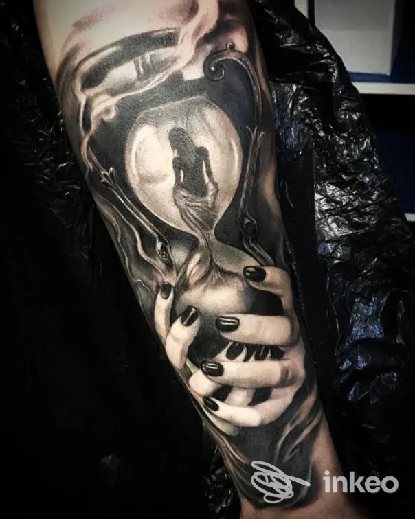 Tatuaggio realistico in bianco e nero su avambraccio con clessidra e mani, Alter Ego Tattoo Studio, Siena.