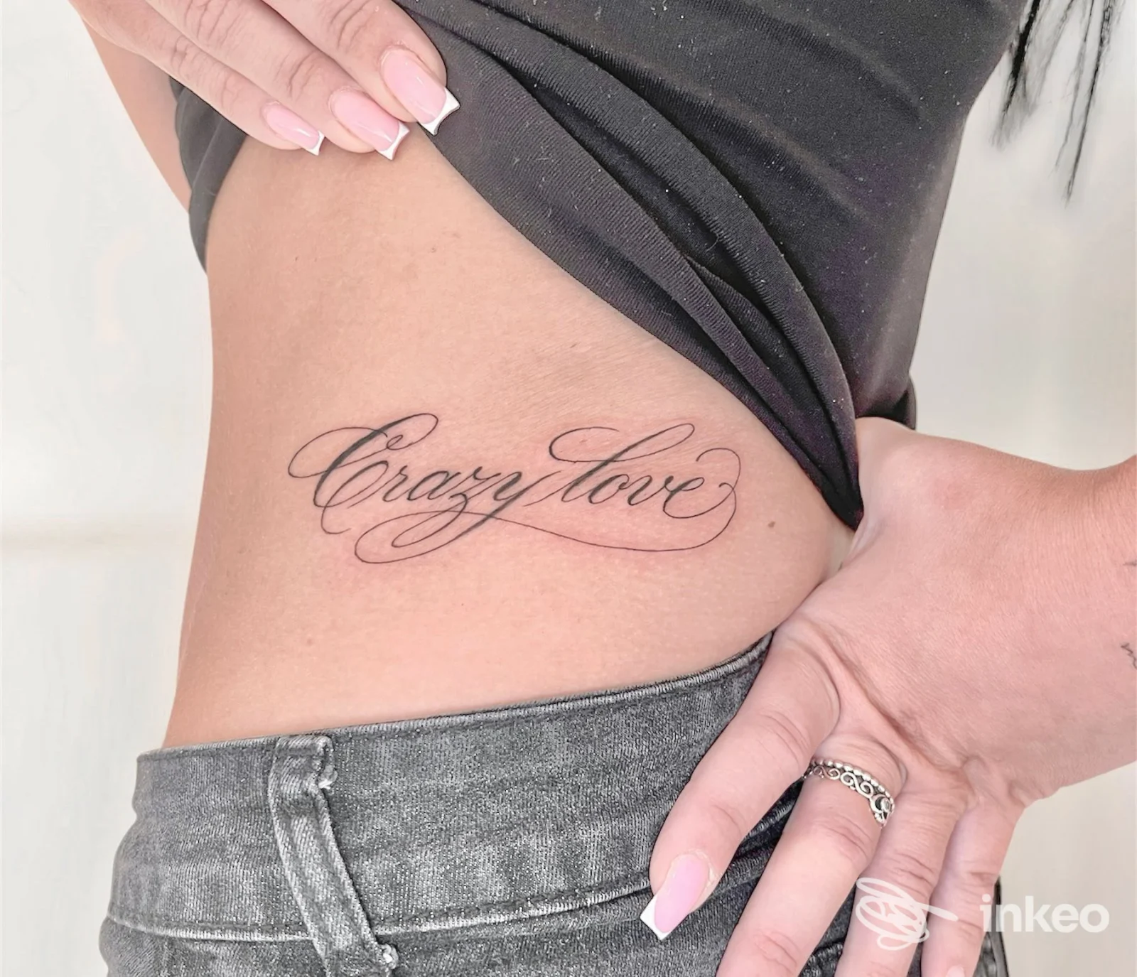 Tattoo calligrafico 'Crazy love' sul fianco destro di una persona, dettaglio del trattamento su pelle in luce naturale. Amnèsia Tattoo Lab, Pistoia.