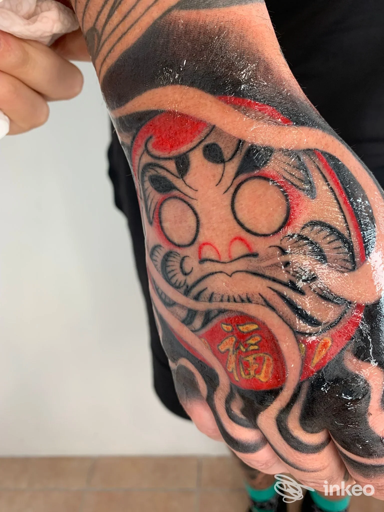 Dorso della mano e polso tatuati con volto stilizzato in nero e rosso, fotografia dello studio Antivist Tattoo a Cascina.