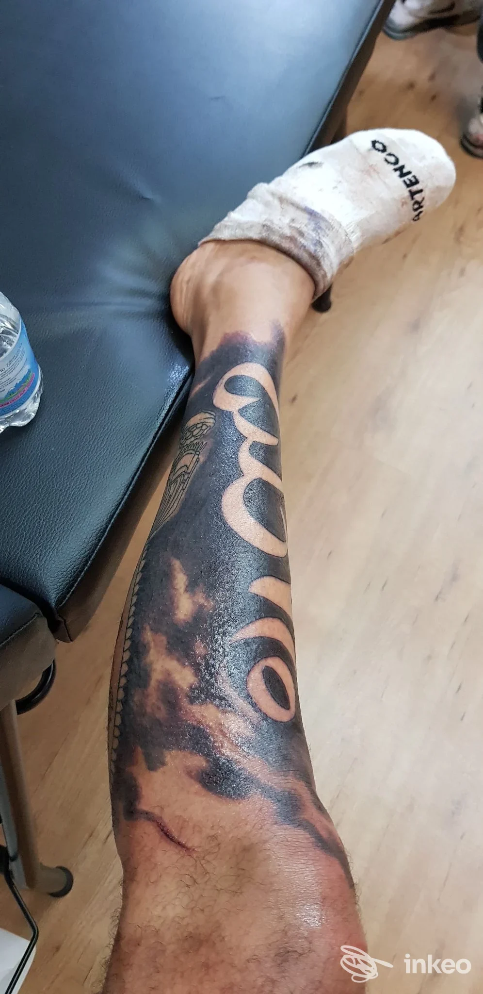 Immagine di un avambraccio sinistro con grande tatuaggio scuro e grafico, parzialmente visibile su sfondo pavimento, senza volto né elementi social. Studio Area Industriale Tattoo a Brescia.