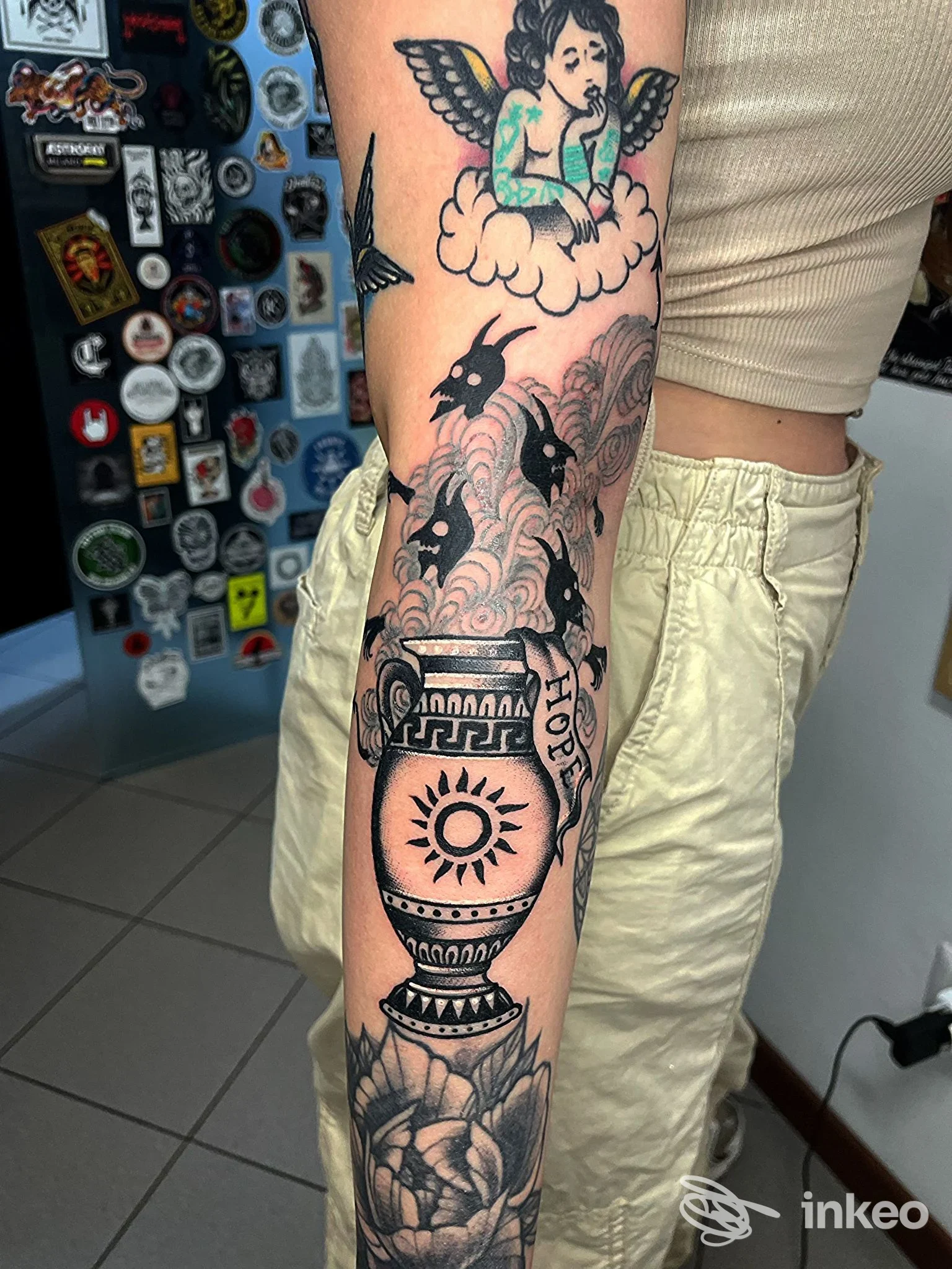 Avambraccio tatuato con urna decorativa, fiori e angelo; foto dallo studio Black Circle Hellectric Tattooing, Figline Valdarno.