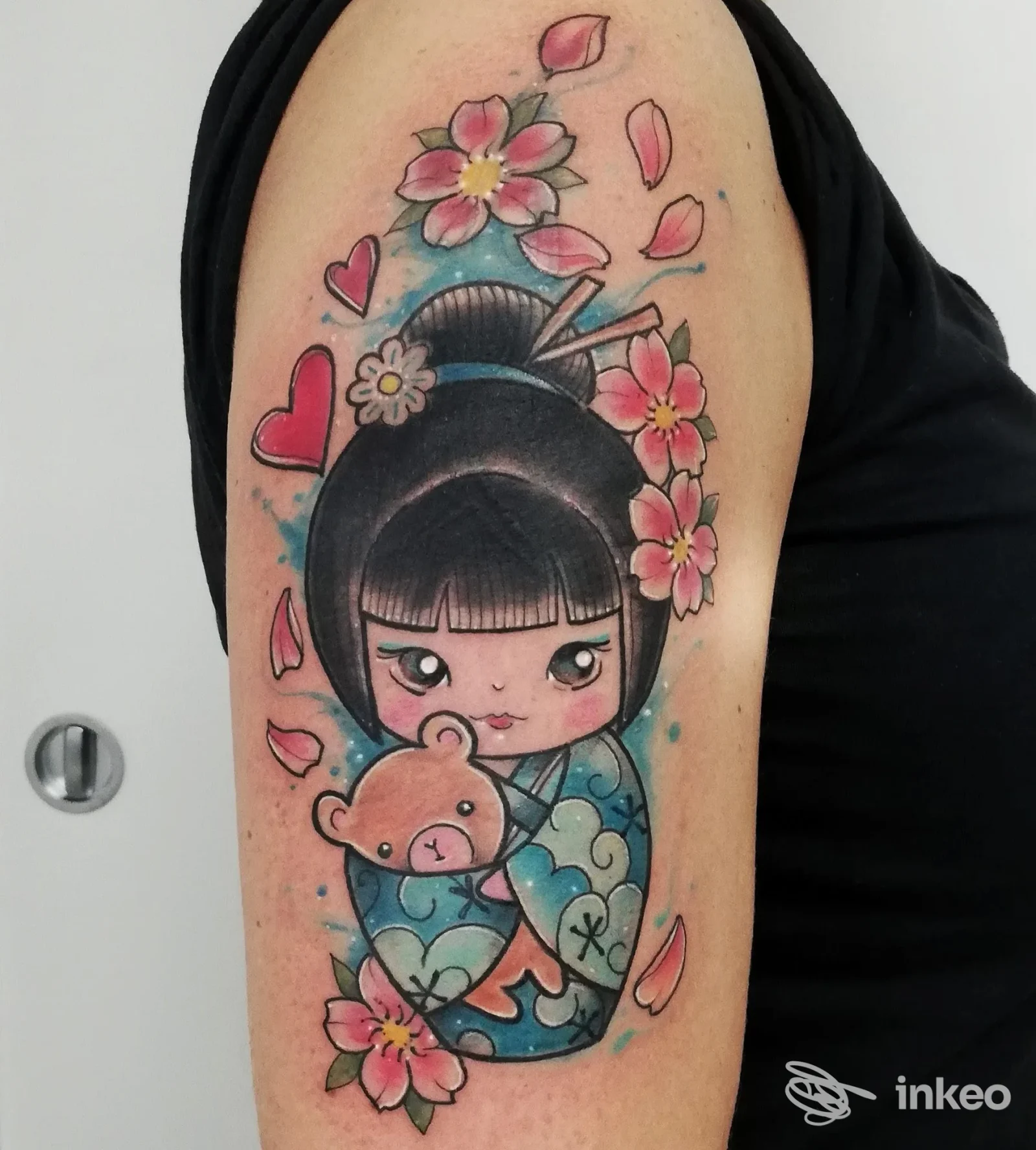 Tatuaggio colorato a tema kokeshi con orsetto e fiori sull'altezza dell'omero, realizzato da Bohemien Tattoo Parlour a Firenze.