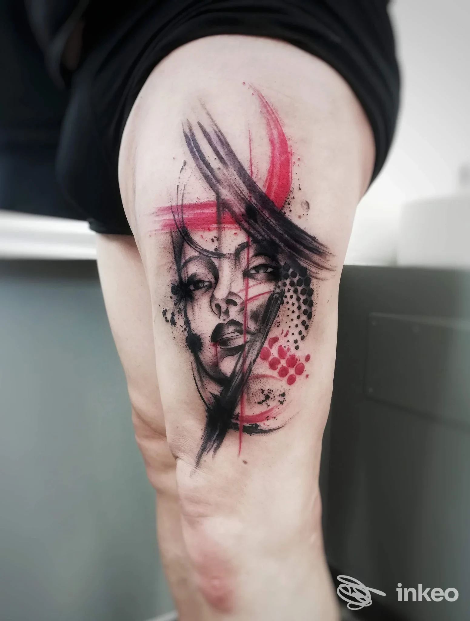 Tatuaggio su coscia con volto stilizzato in nero e rosso, Bohemien Tattoo Parlour, Firenze.