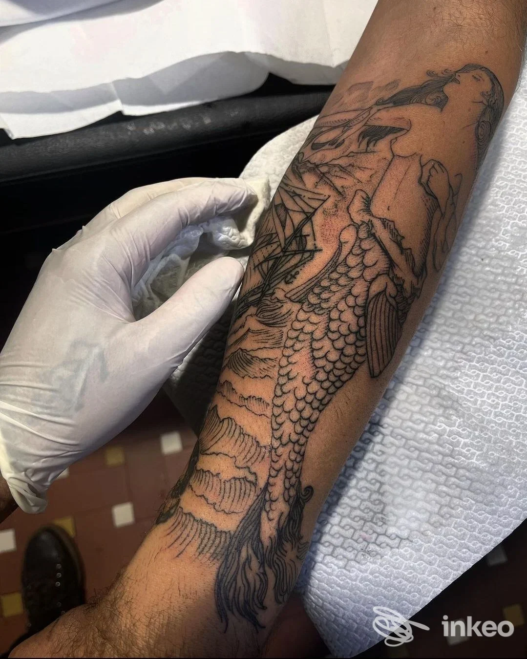 Avambraccio tatuato con soggetto marino, foto di C H Z Tattooing a Massa mentre l'operatore indossa un guanto pulente.