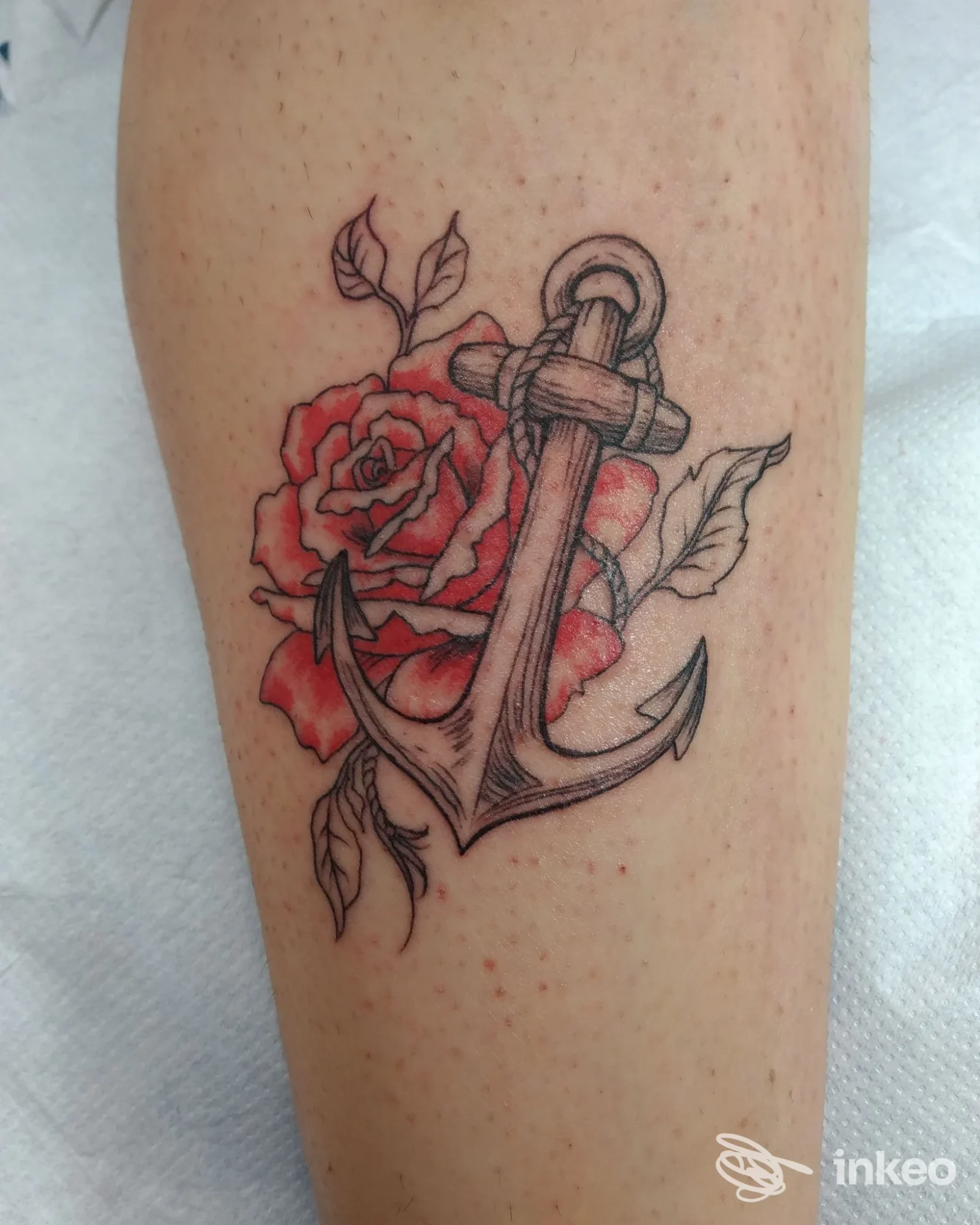 Tatuaggio colore nero e rosso di un'ancora sovrapposta a una rosa sul polpaccio. Cannella Elena - Tattoo Art Shop, Castellina Marittima.