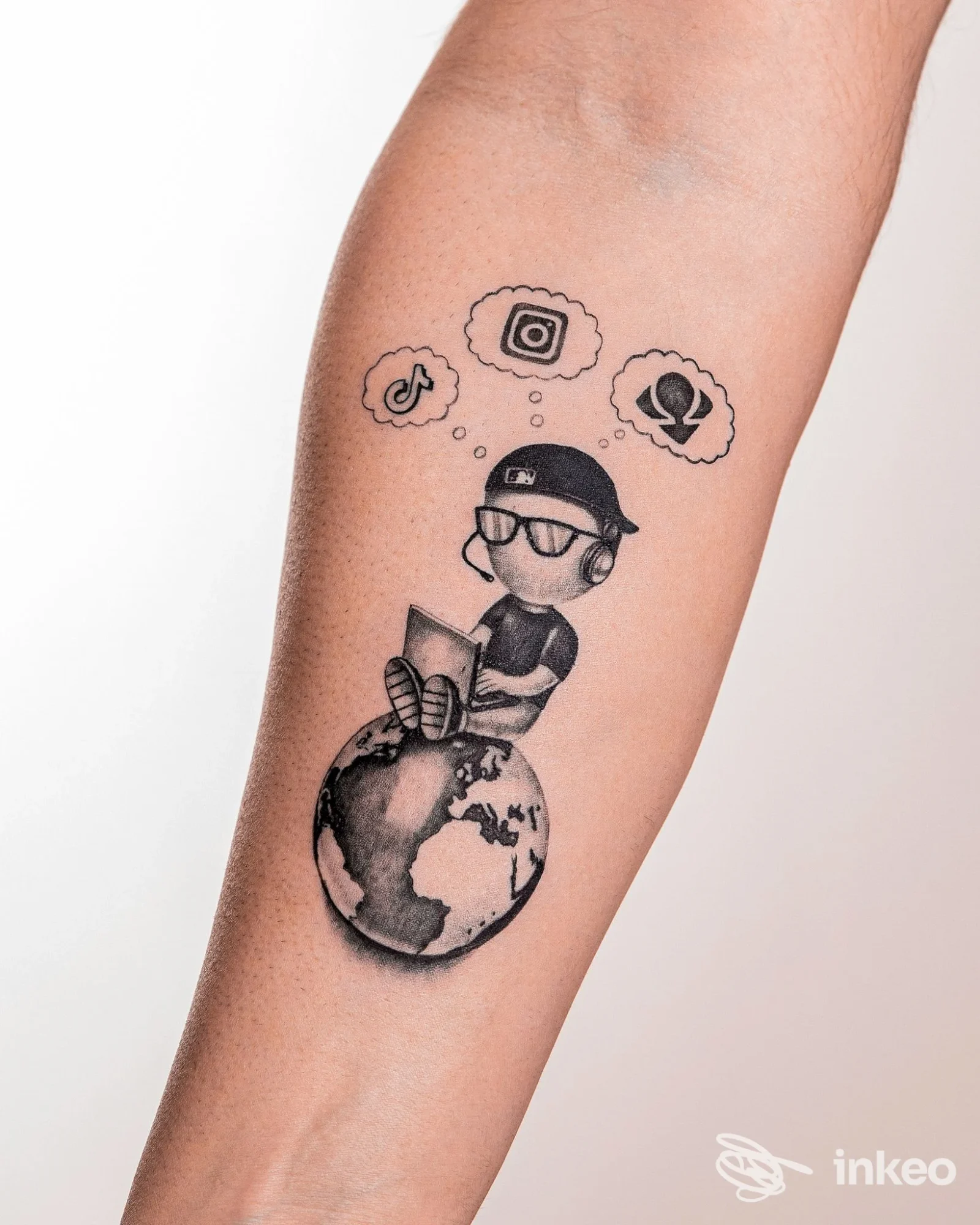 Tatuaggio sul braccio raffigurante una figura stilizzata seduta su una mappa del mondo, che legge un libro, con nuvole di pensiero contenenti icone di app digitali.