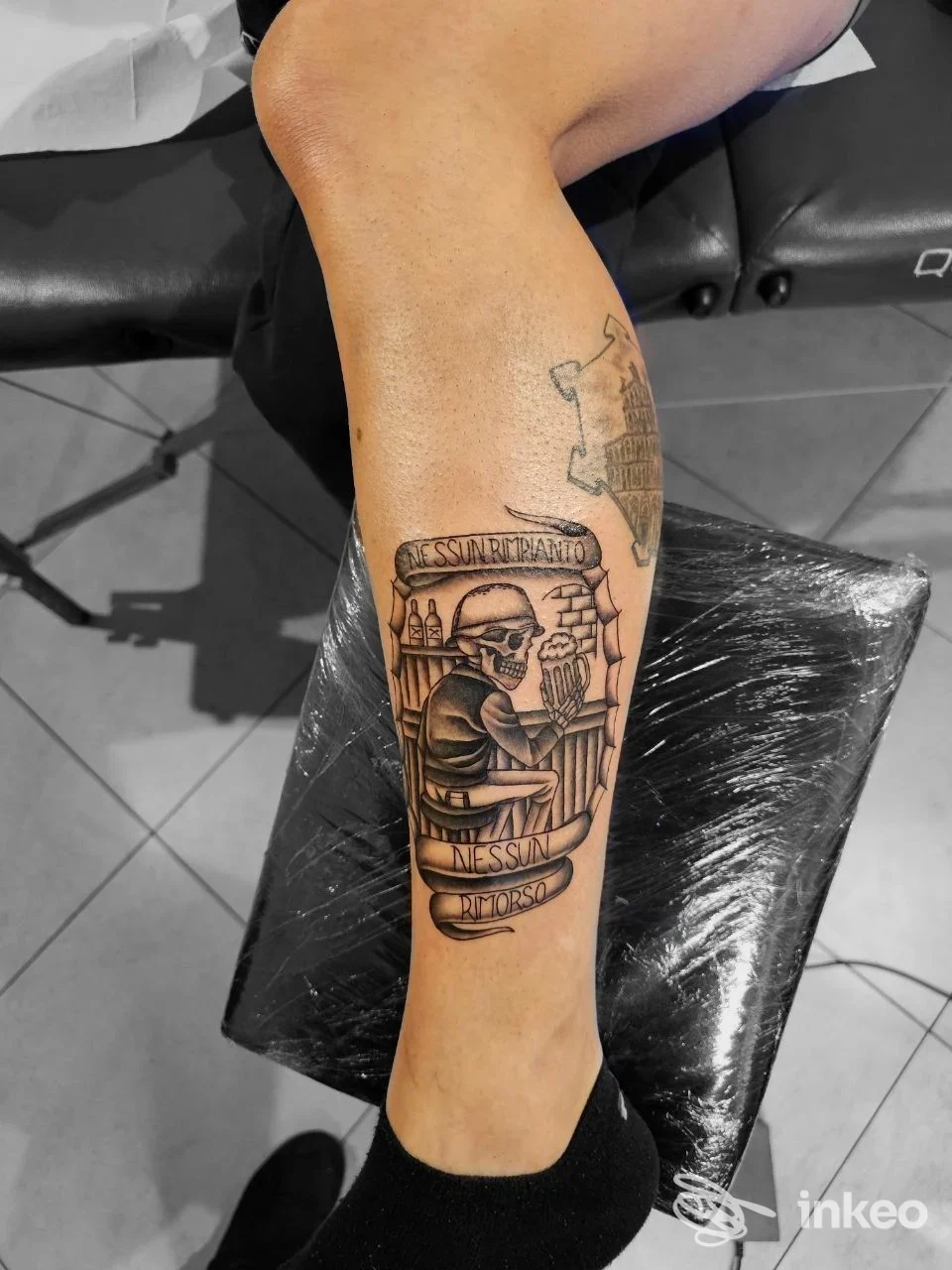 Tatuaggio black & grey sul polpaccio realizzato da Dark Romantics Tattoo a Lucca, soggetto scheletro con ringhiera e striscione.