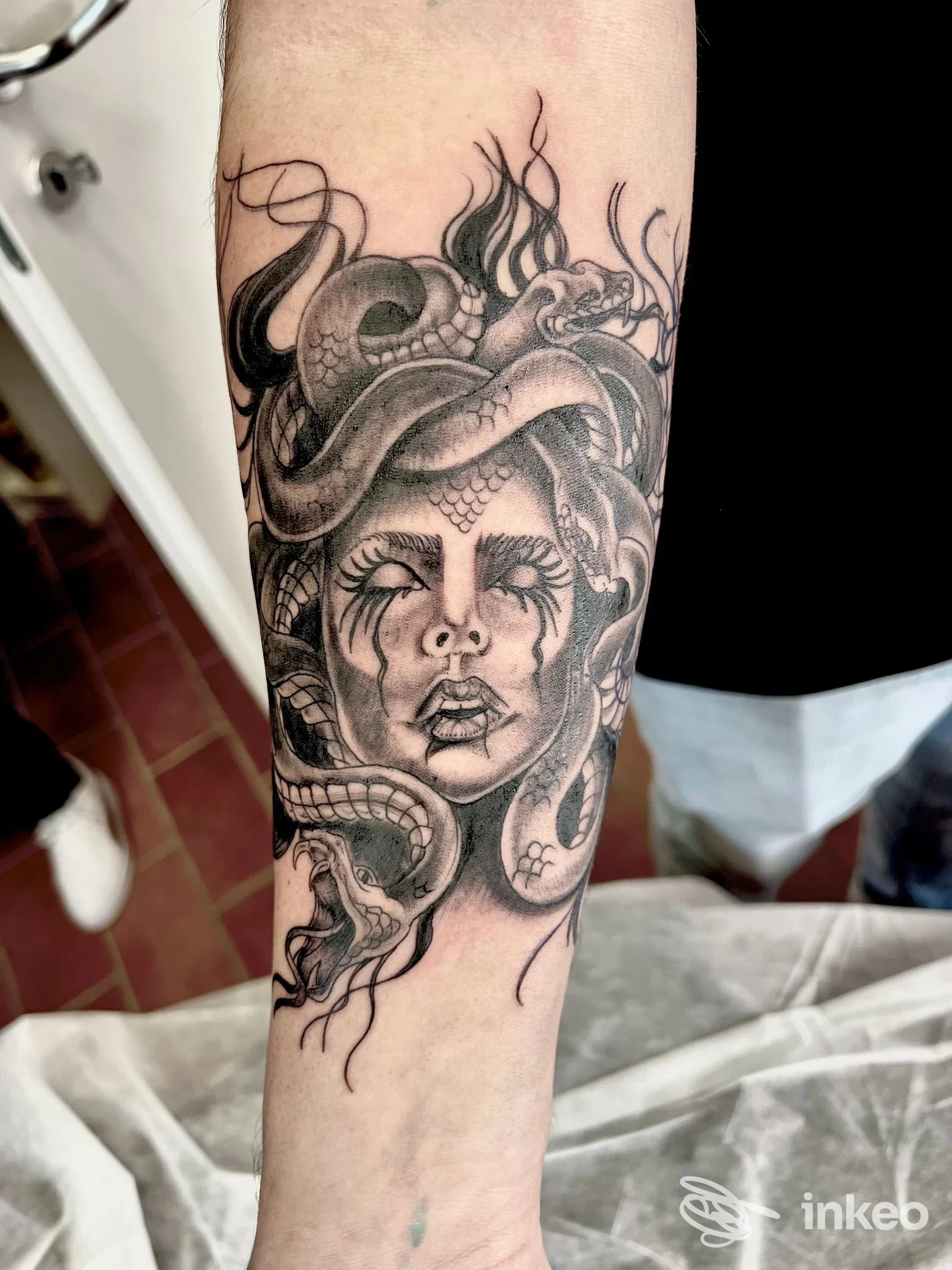 Tattoo in bianco e nero su avambraccio sinistro: una testa femminile avvolta da serpenti, realizzazione tatuata sulla pelle, senza testo o overlay visivo.