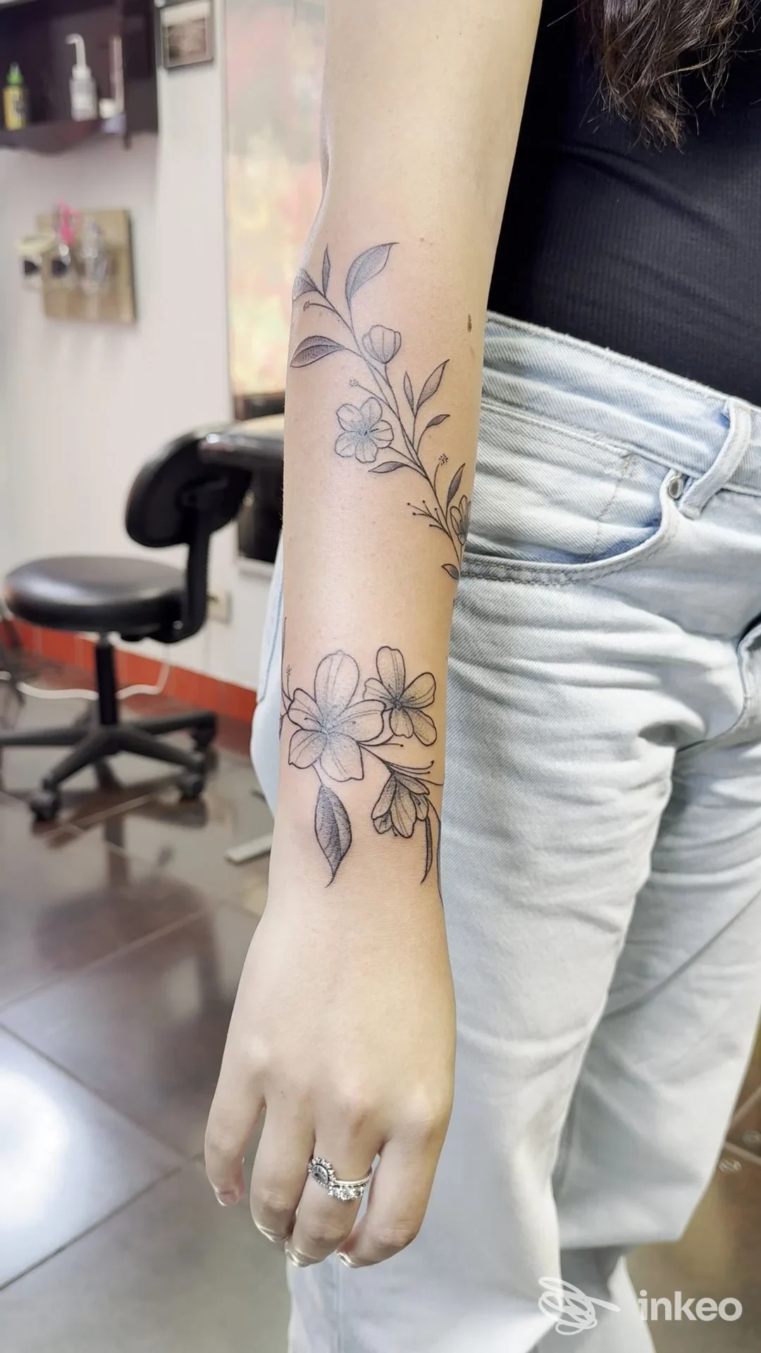 Primo piano dell'avambraccio con tatuaggio floreale lineare realizzato da Energia Tattoo Studio a Livorno, ambiente di studio sullo sfondo.