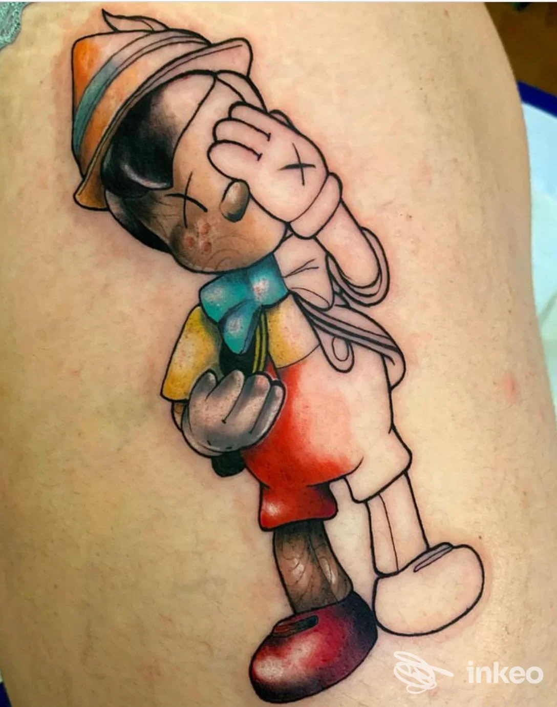 Tatuaggio colorato di un Pinocchio stilizzato sulla coscia, fotografato per Factory Tattoo Studio a Pisa.