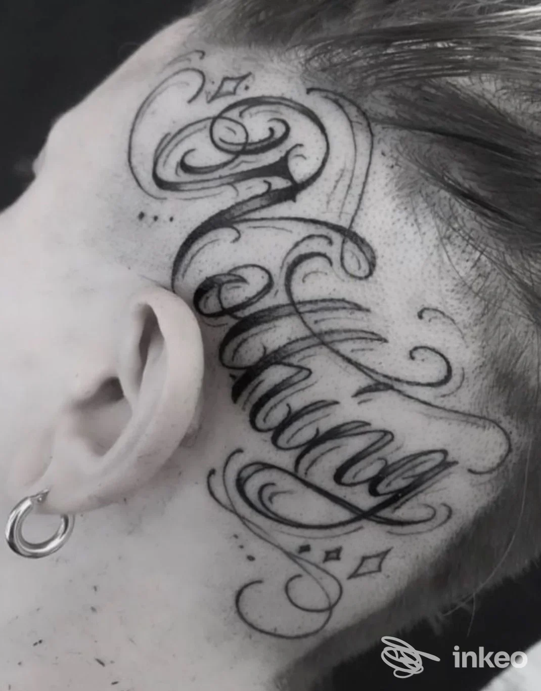 Primo piano di un tatuaggio calligrafico nero sul lato della testa vicino all'orecchio, foto fornita da Factory Tattoo Studio a Pisa.