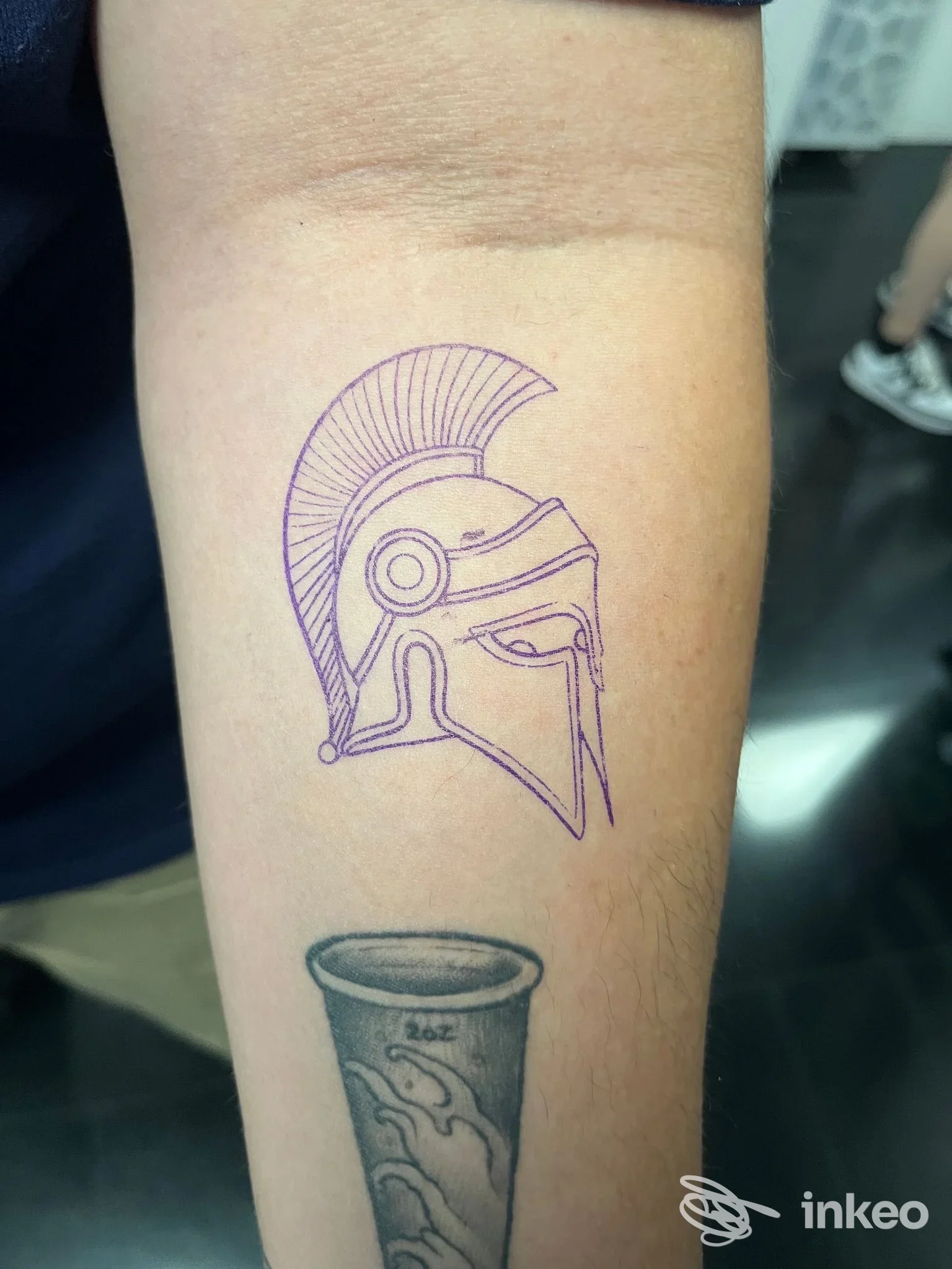 Avambraccio con stencil viola a forma di elmo sopra tatuaggio esistente; immagine fornita da Florence City Ink Tattoo Studio, Firenze.