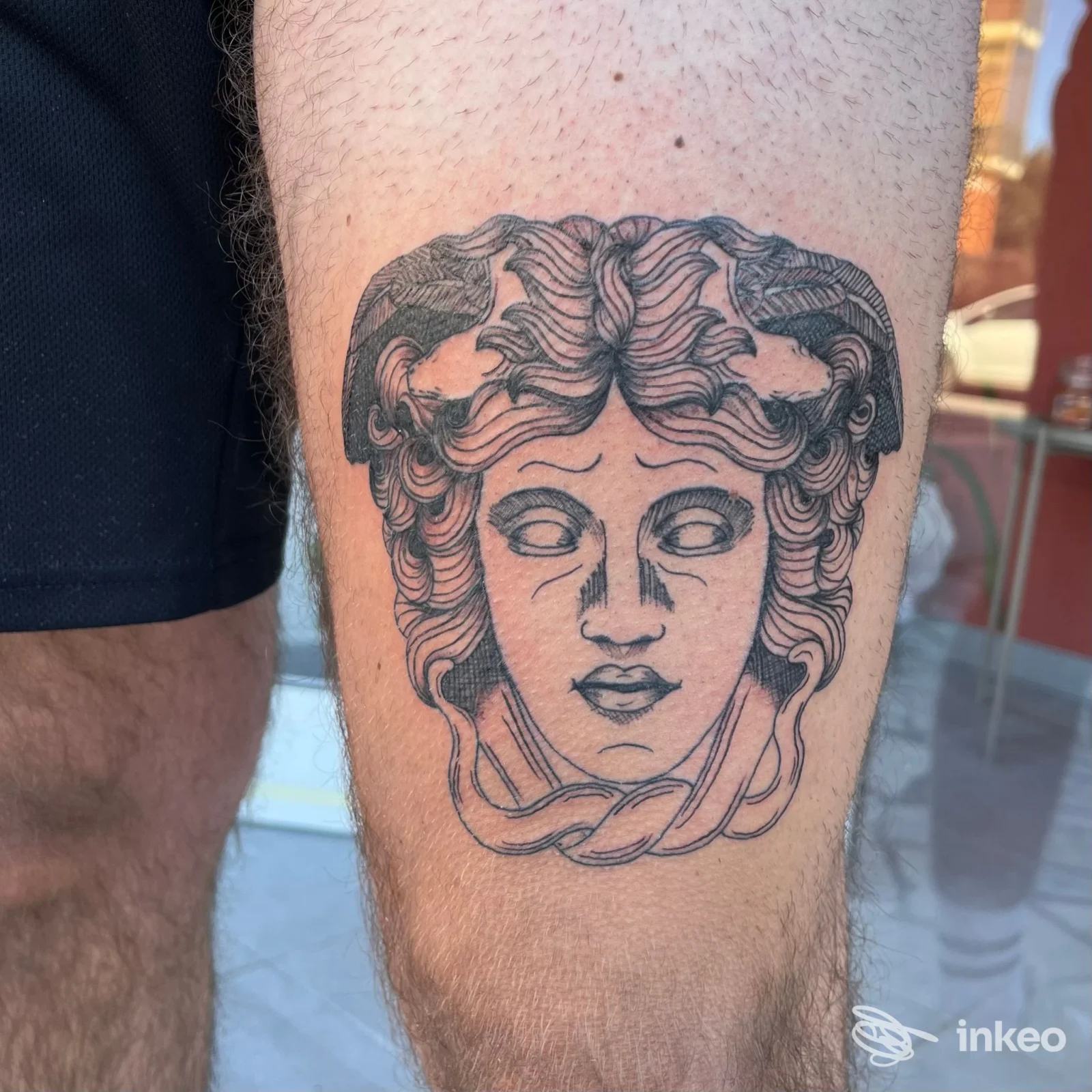 Tatuaggio a inchiostro nero di un volto stilizzato sulla coscia, foto inviata da GINGER TATTOO a Carrara.