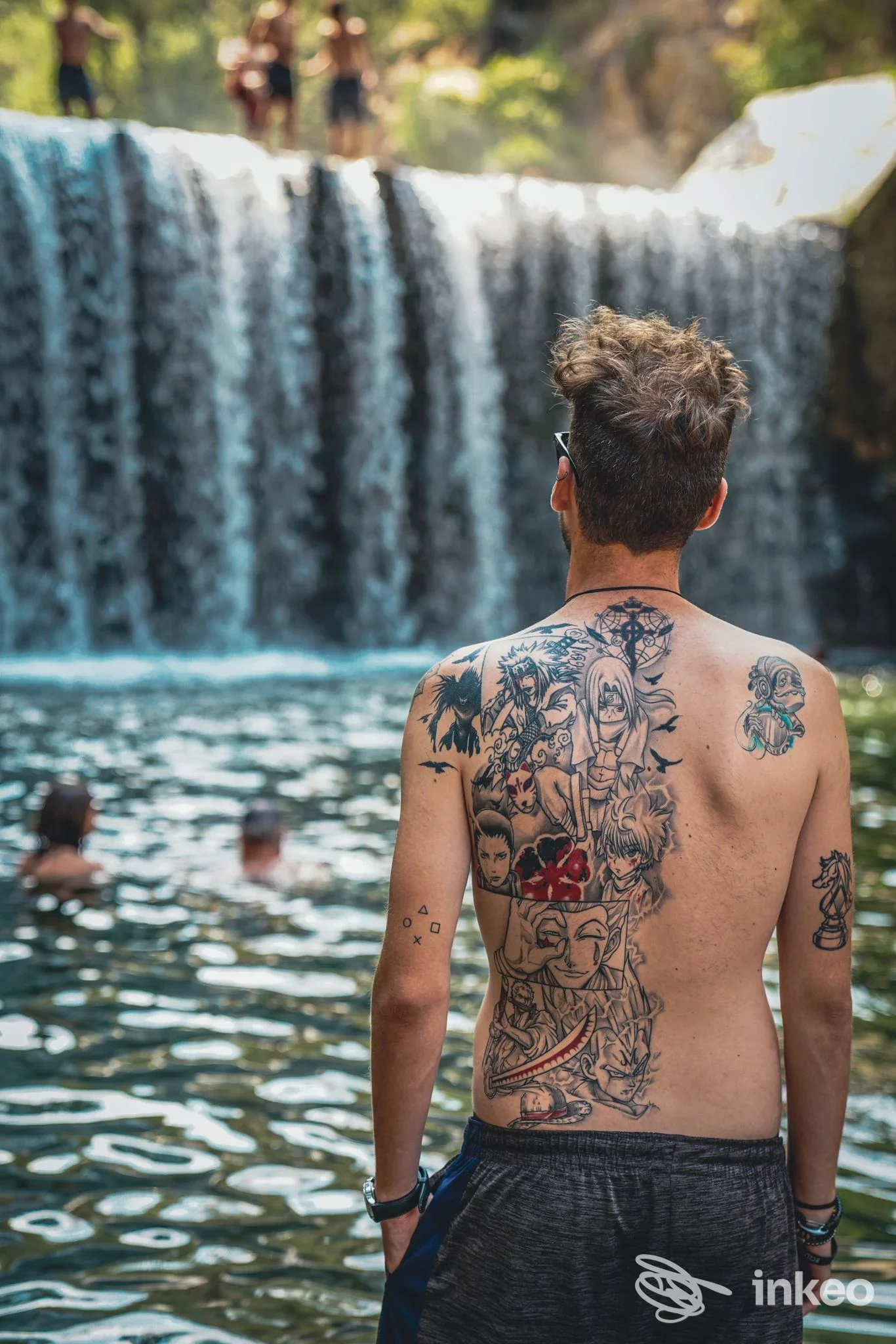 Uomo di schiena con ampio tatuaggio sulla schiena, in acqua davanti a una cascata. ARTCORE Tattoo & Piercing, Lastra a Signa.