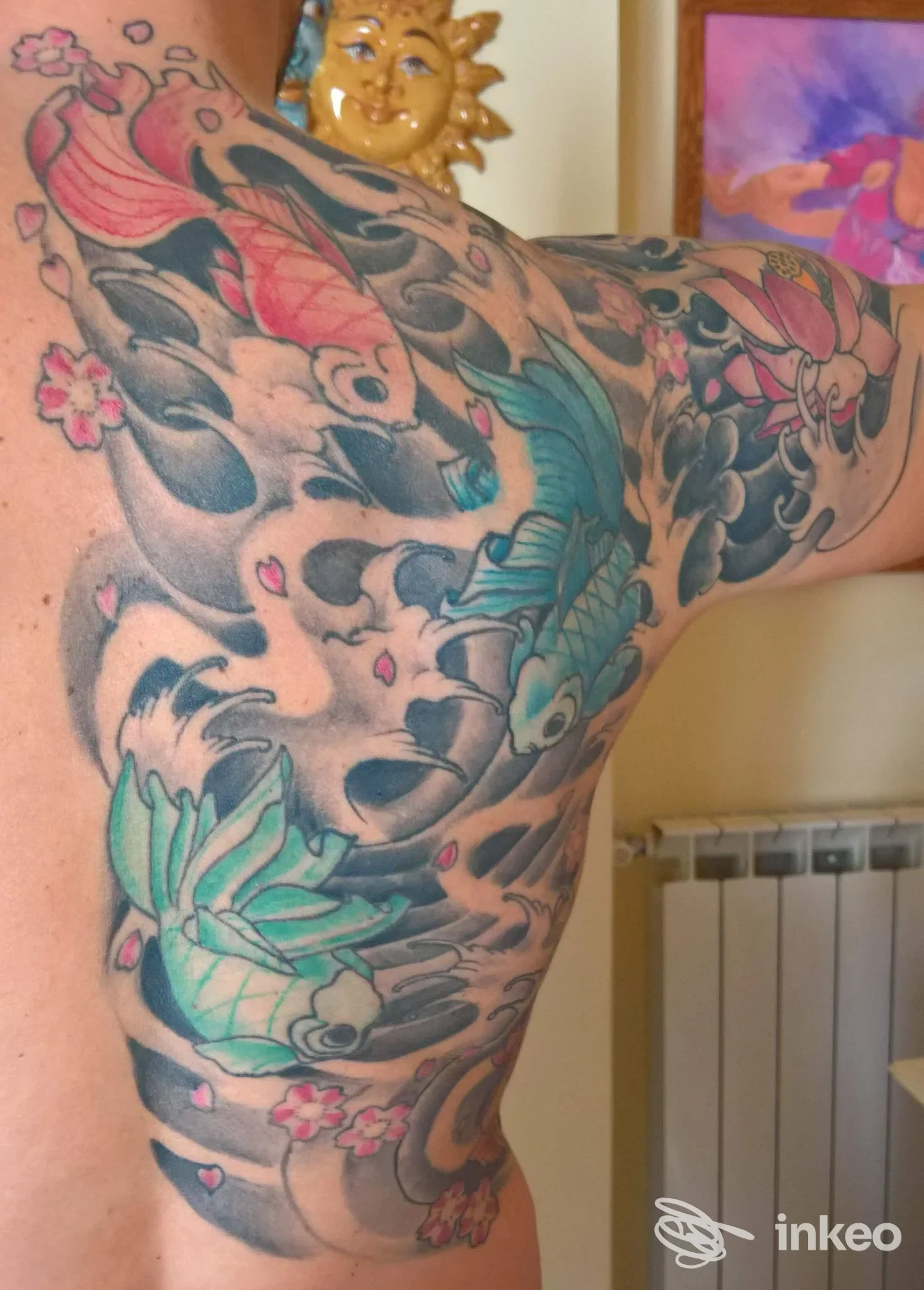 Ampia composizione tatuata su spalla e dorso con carpe, onde e fiori; foto inviata da Admiral Tattoo a Massa.