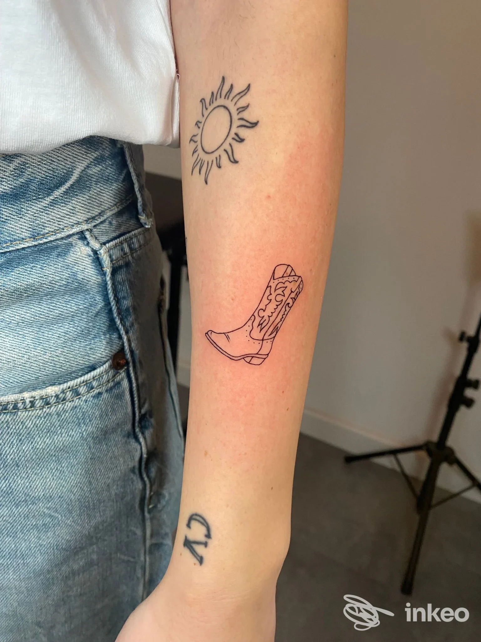 Avambraccio con tatuaggi in linea: sole vicino al gomito e stivale western sul braccio, foto di Abra tattoo Firenze.
