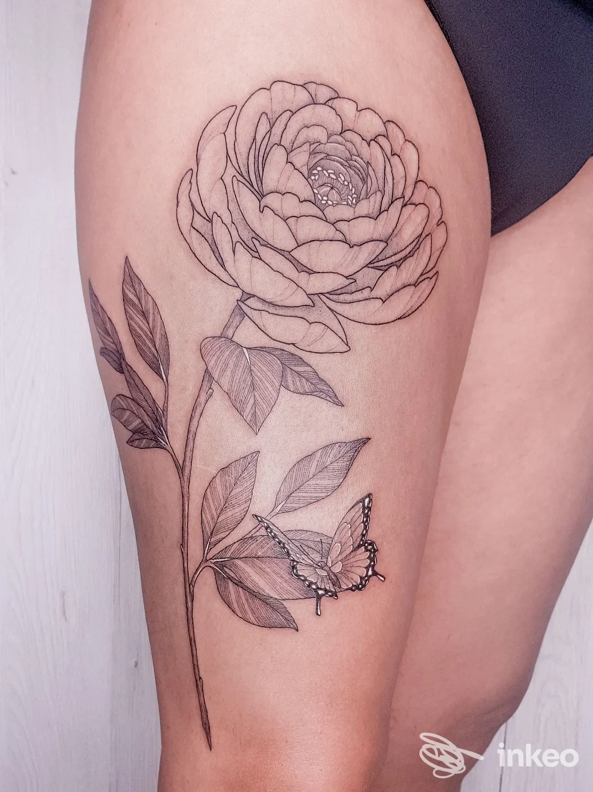 Grande tatuaggio botanico con fiore e farfalla sulla coscia, realizzato da Cadillac Ranch Tattoo a Firenze.