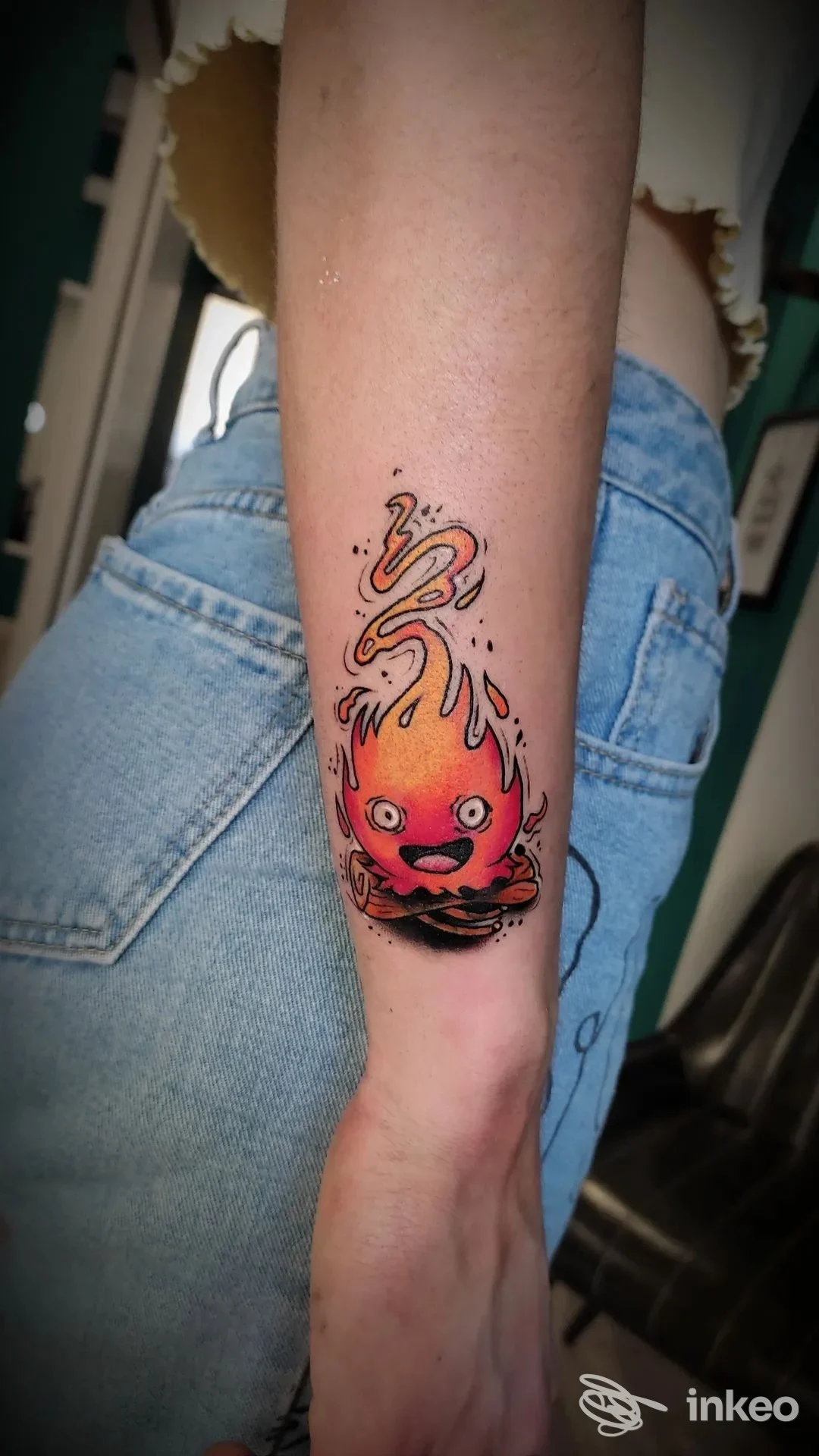 Tatuaggio su avambraccio di una fiamma stilizzata con occhi e bocca in rosso e nero. Al Tattoo Studio, Firenze.