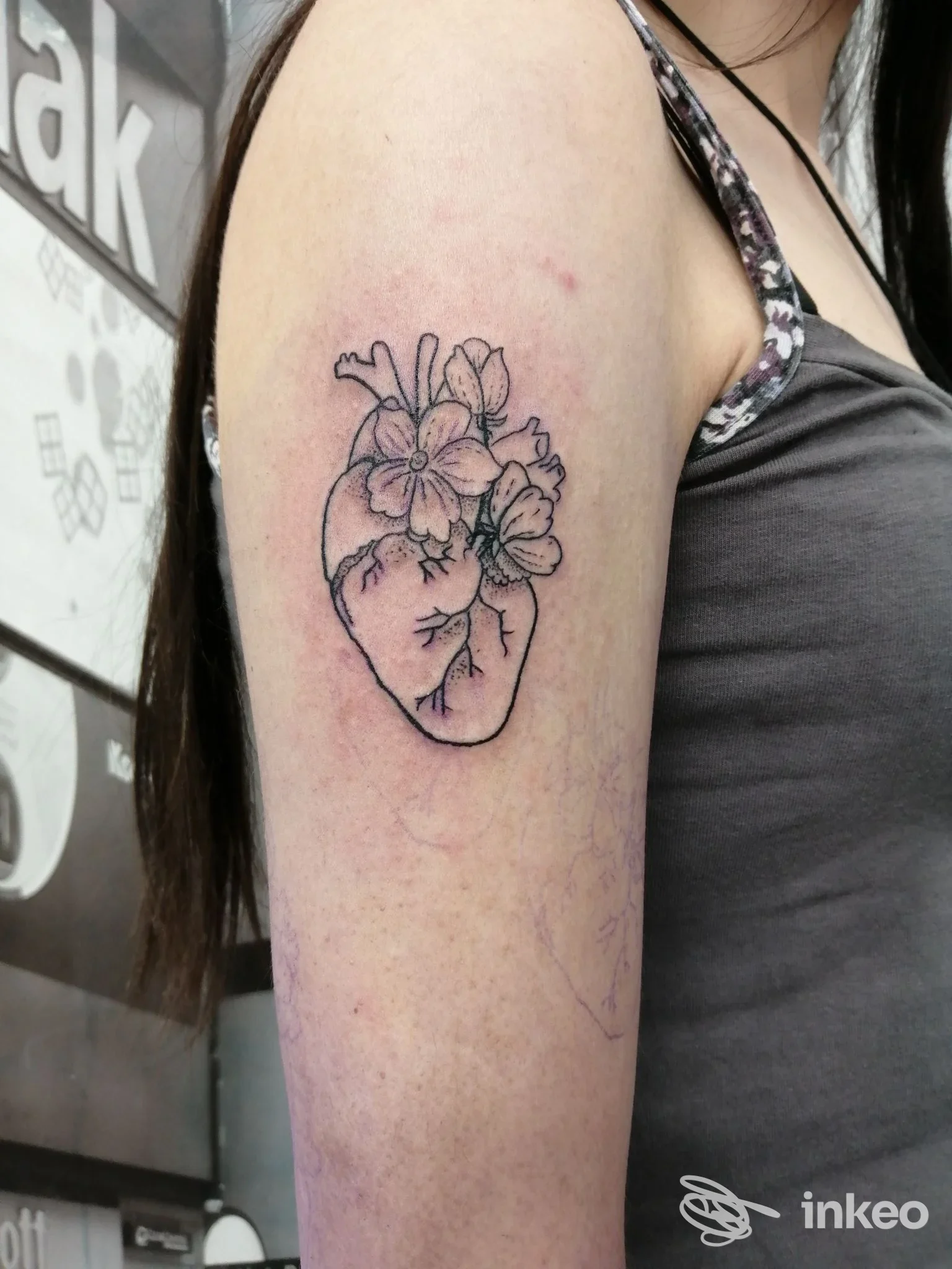 Tatuaggio su alto braccio: cuore anatomico nero con fiori, foto scattata nello studio Cuore Nero - Tattoo e Piercing a Livorno.