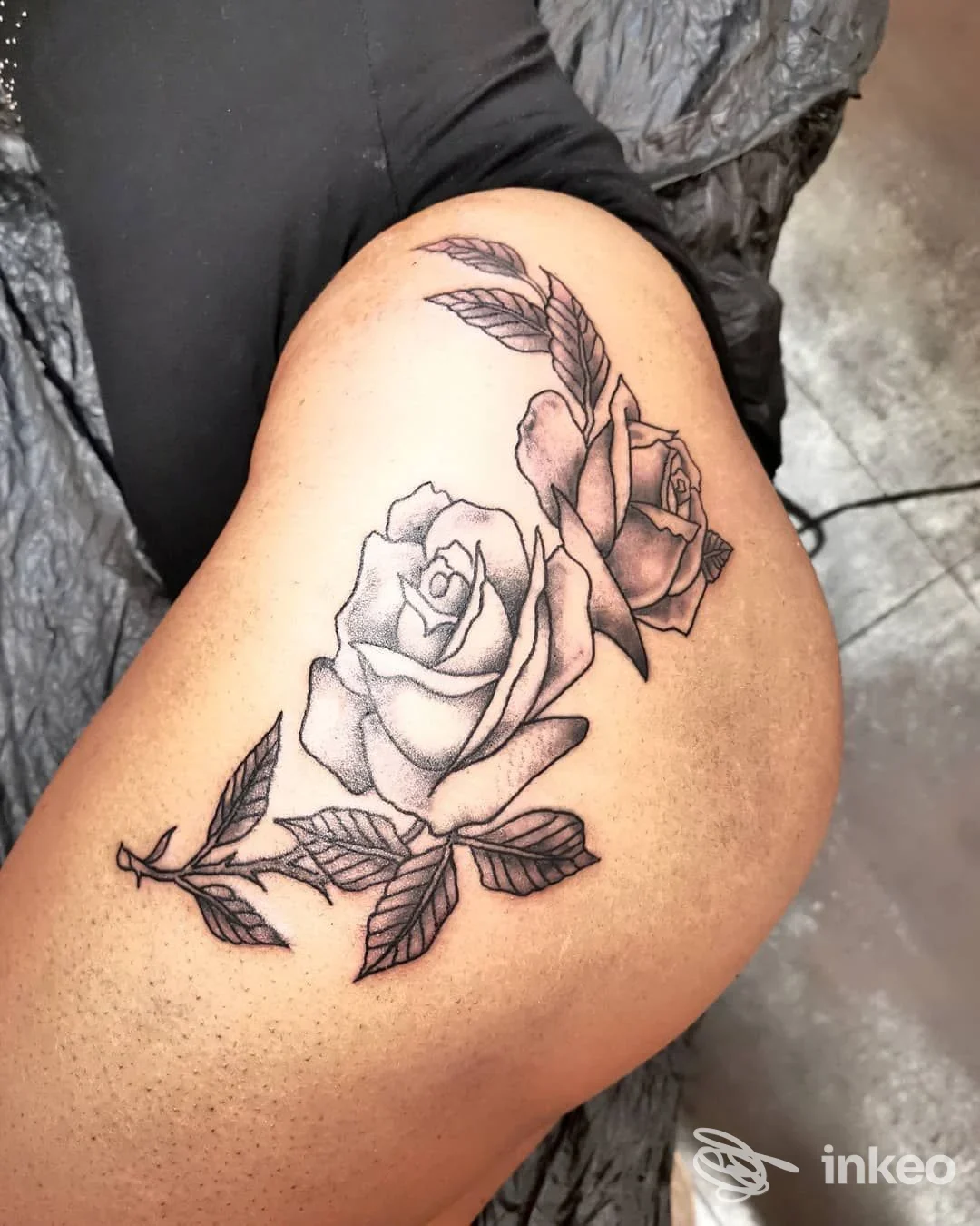 Tatuaggio floreale in nero con due rose e foglie sulla parte alta della coscia, foto da ElCagliador Tattoo Studio, Firenze.