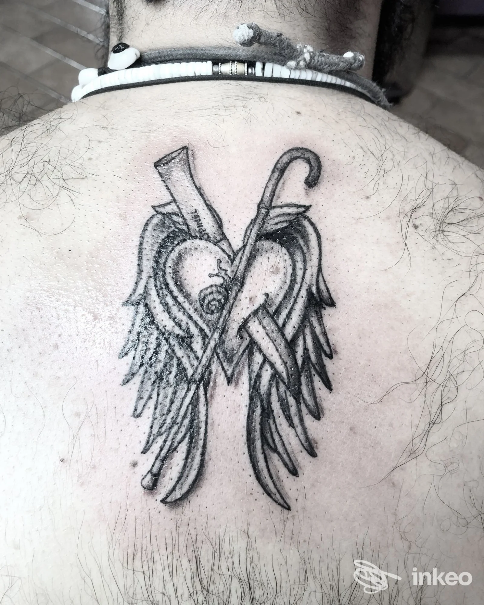 Tatuaggio bianco e nero con cuore, ali e bastoni sulla parte alta della schiena. Freedom Tattoo, Pistoia.